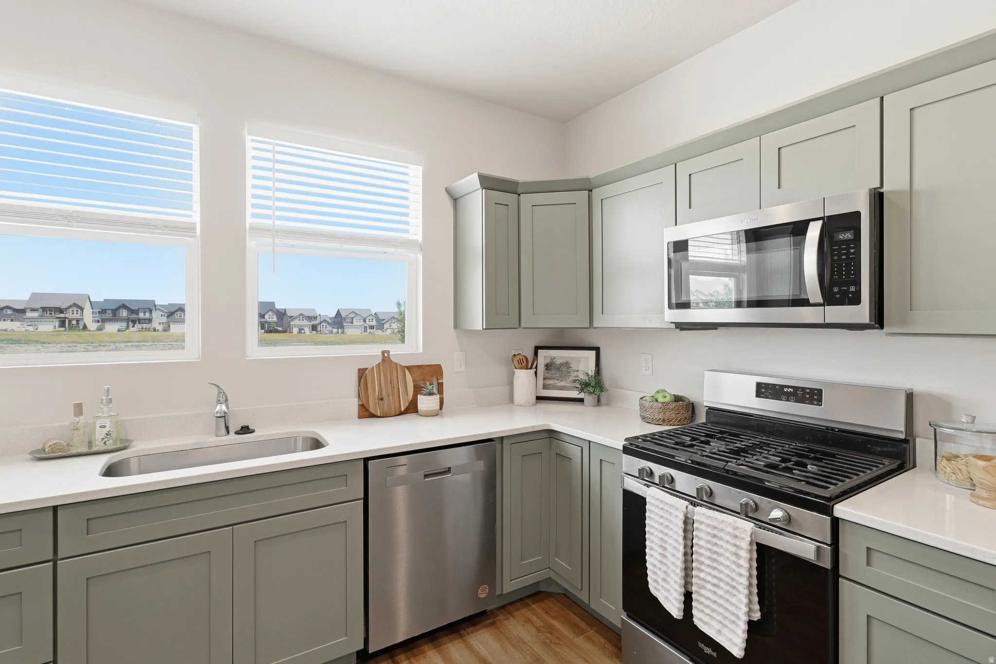 Kitchen featuring sage-green cabinetry, stainless steel appliances, white countertops, and wood-finish flooring