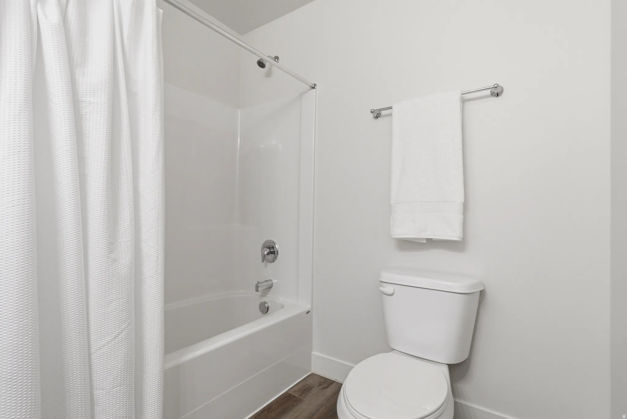 Tub-shower combination with white surround, chrome fixtures, and wood-finish flooring