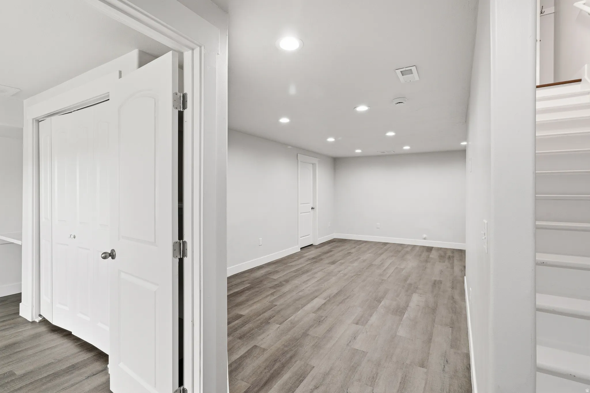 Spacious room featuring wood-finish flooring, recessed lighting, white walls, and a closet with bifold doors