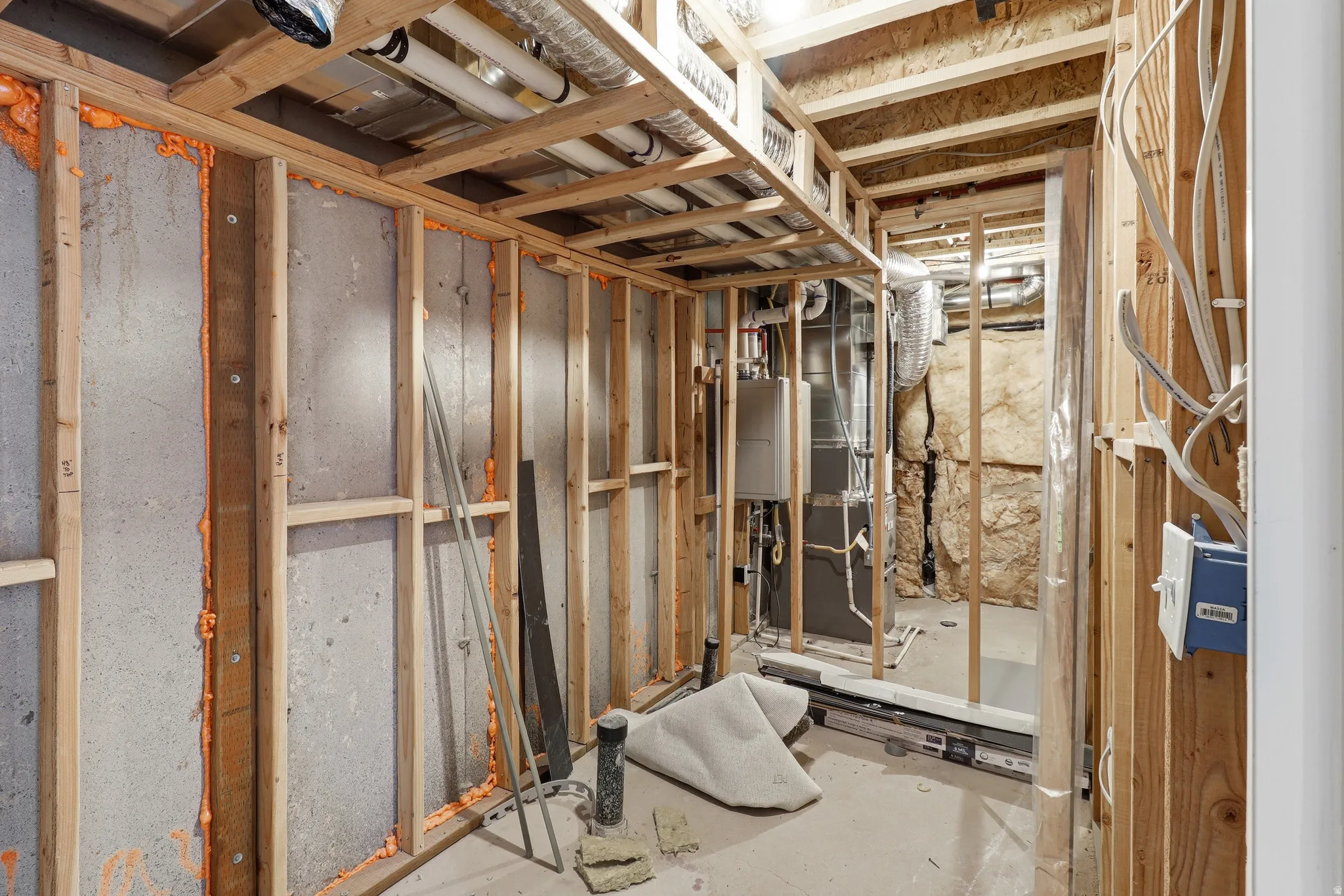 Unfinished basement space featuring exposed wood framing, concrete foundation walls with spray foam insulation, and visible plumbing and electrical infrastructure