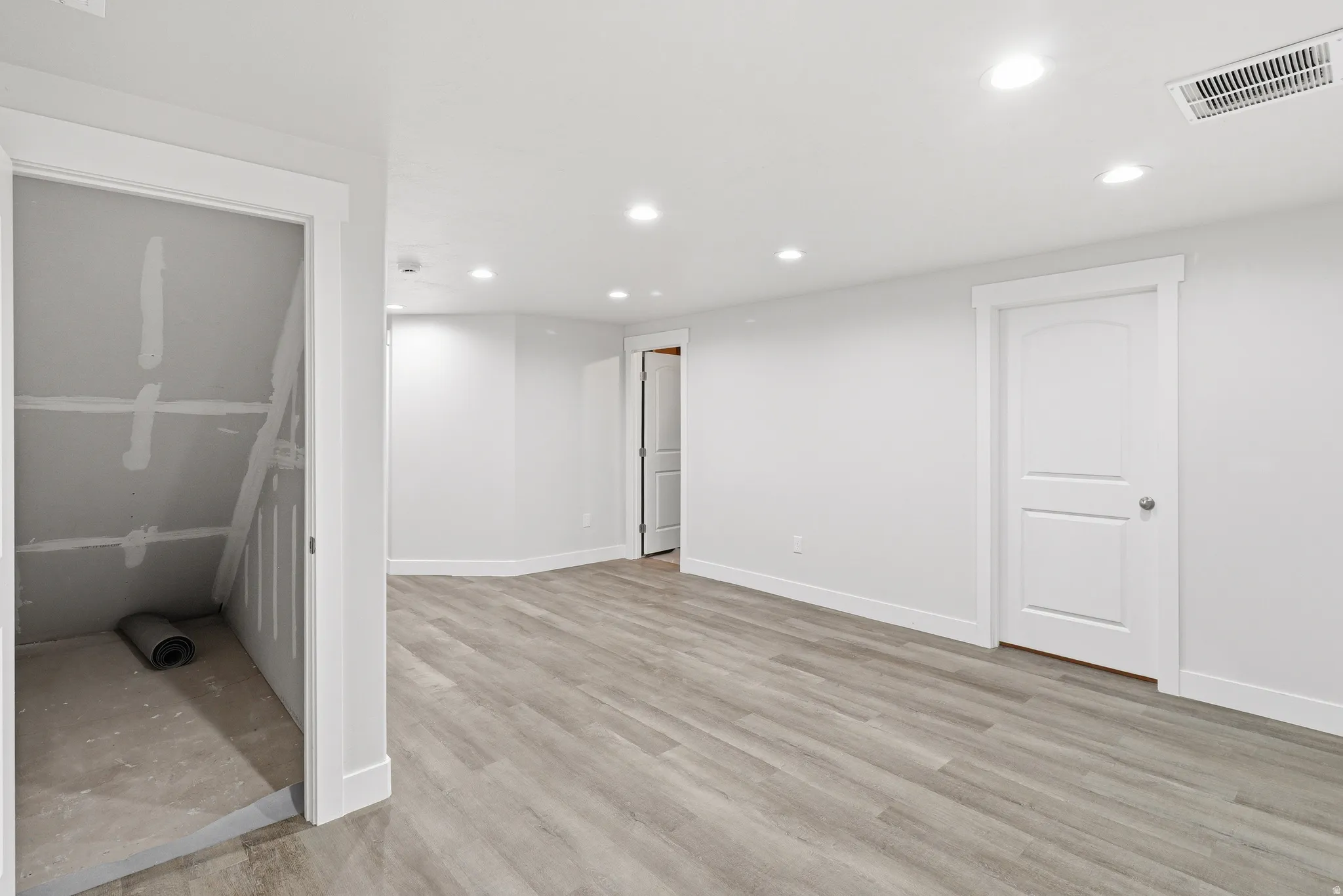 Spacious room featuring wood-finish flooring, recessed lighting, and white baseboards