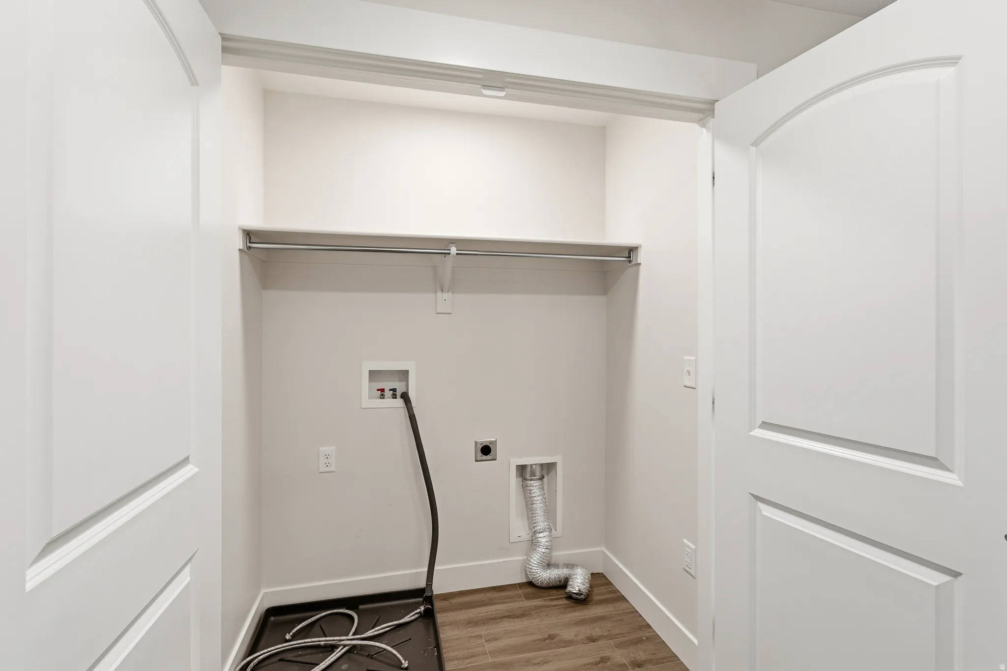 Dedicated laundry closet featuring wood-finish flooring, a metal hanging rod, and a high-set shelf