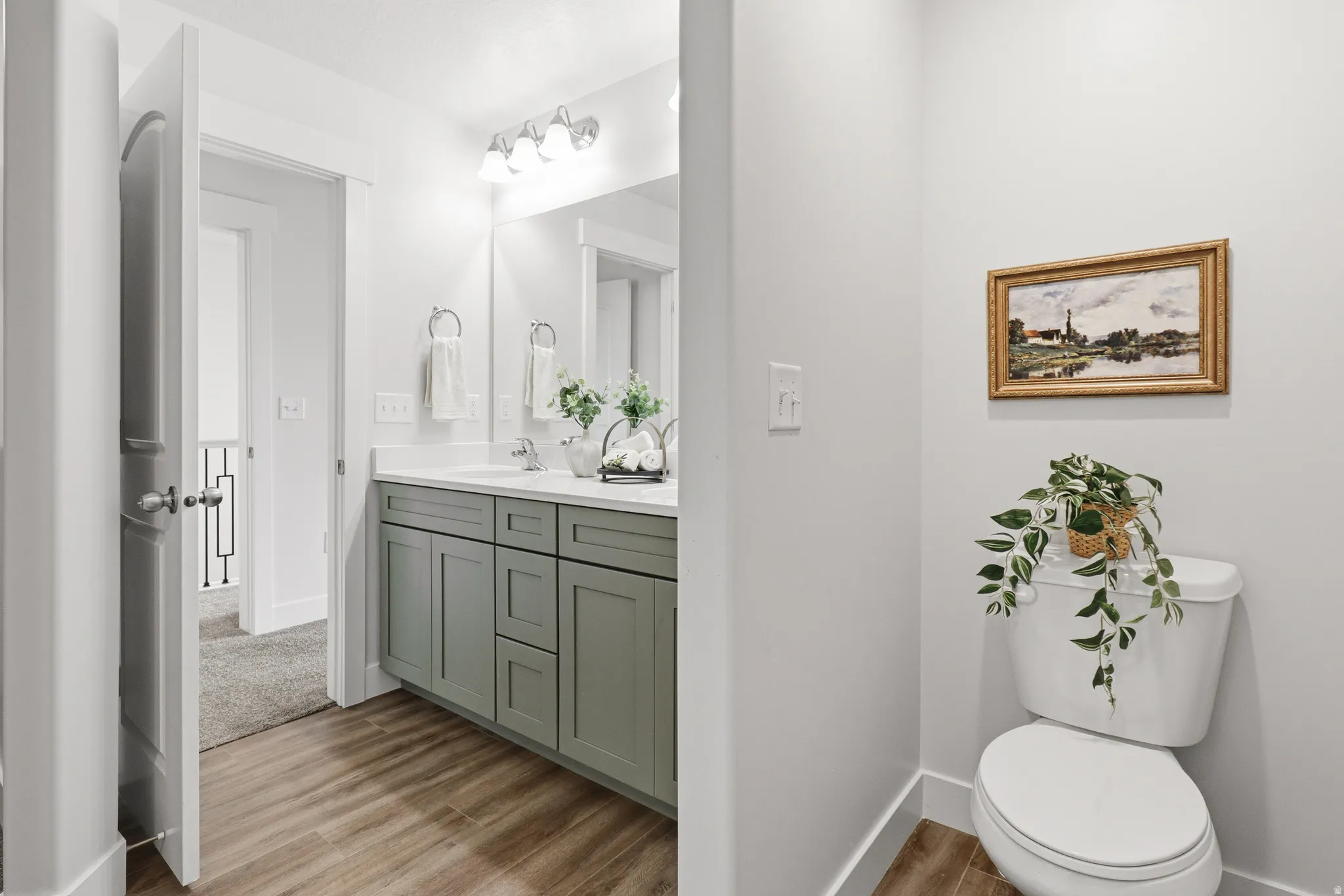 Bathroom featuring a double vanity with light green cabinetry, white countertops, dual undermount sinks, wood-finish flooring, and a wall-mounted light fixture