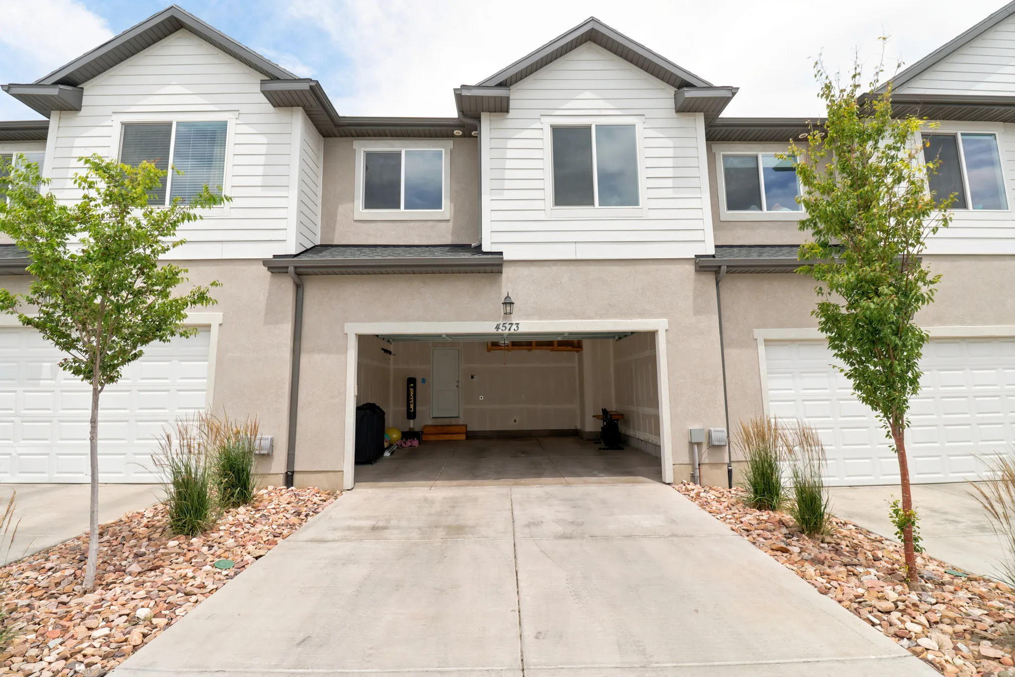 Contemporary townhome exterior featuring light siding and stucco, a dark roofline, and a prominent two-car garage