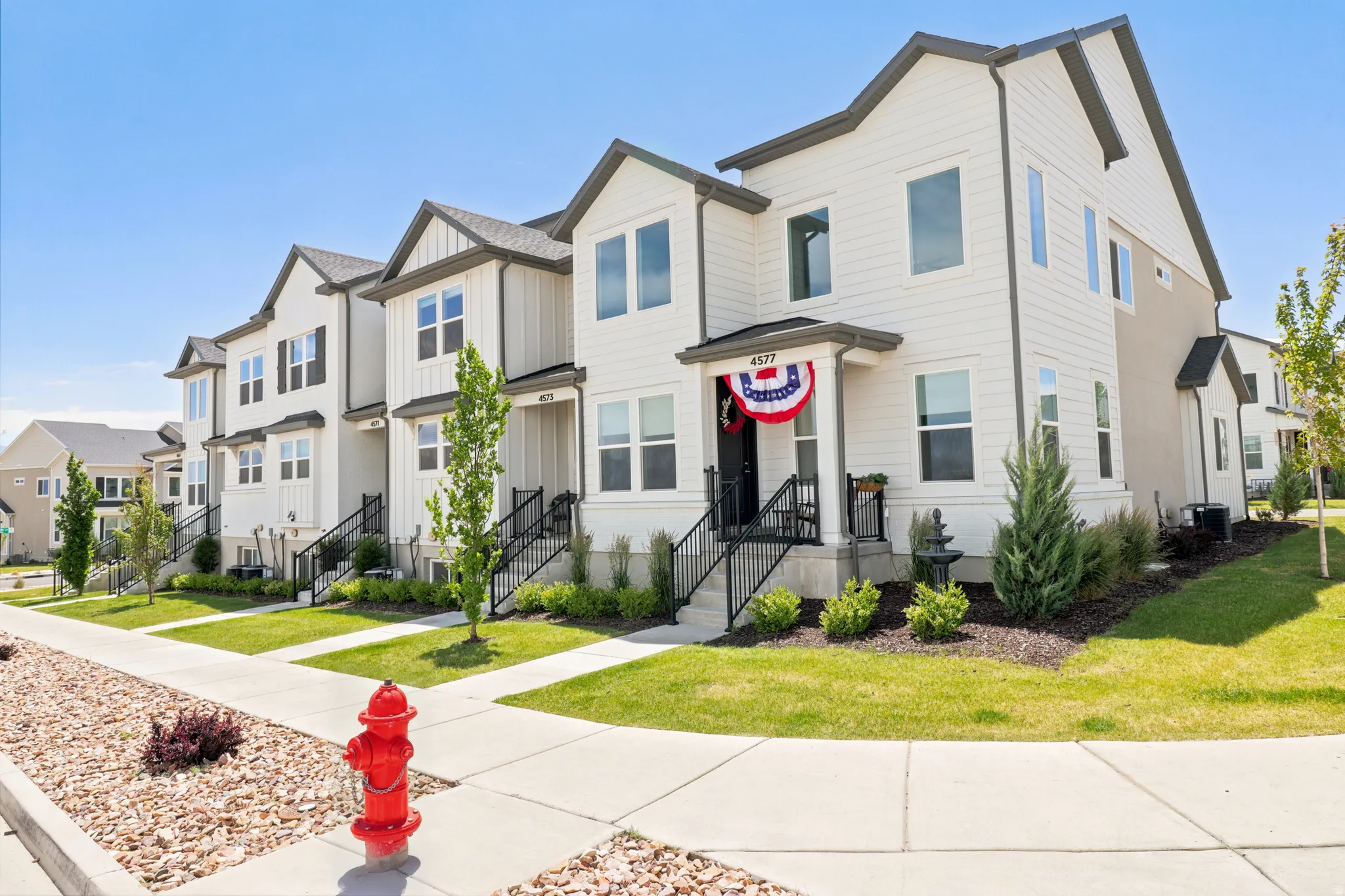 Modern townhome exterior featuring light-colored siding, dark trim, and a covered porch entry