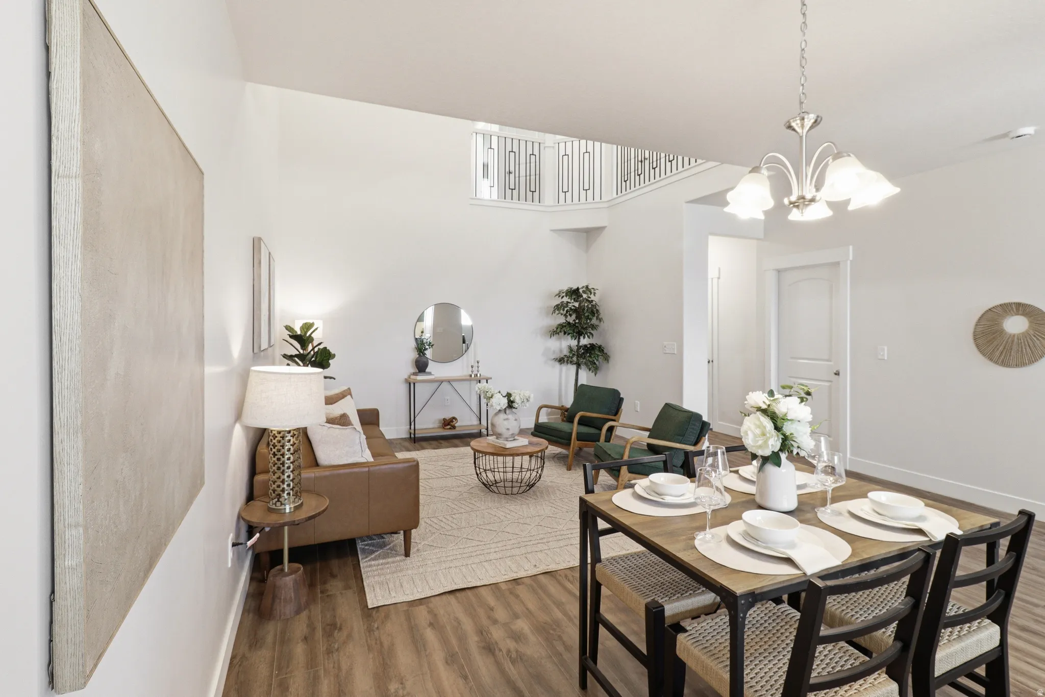 Open-concept living and dining area featuring wood-finish flooring, a contemporary chandelier, and a second-level railing with decorative metal spindles