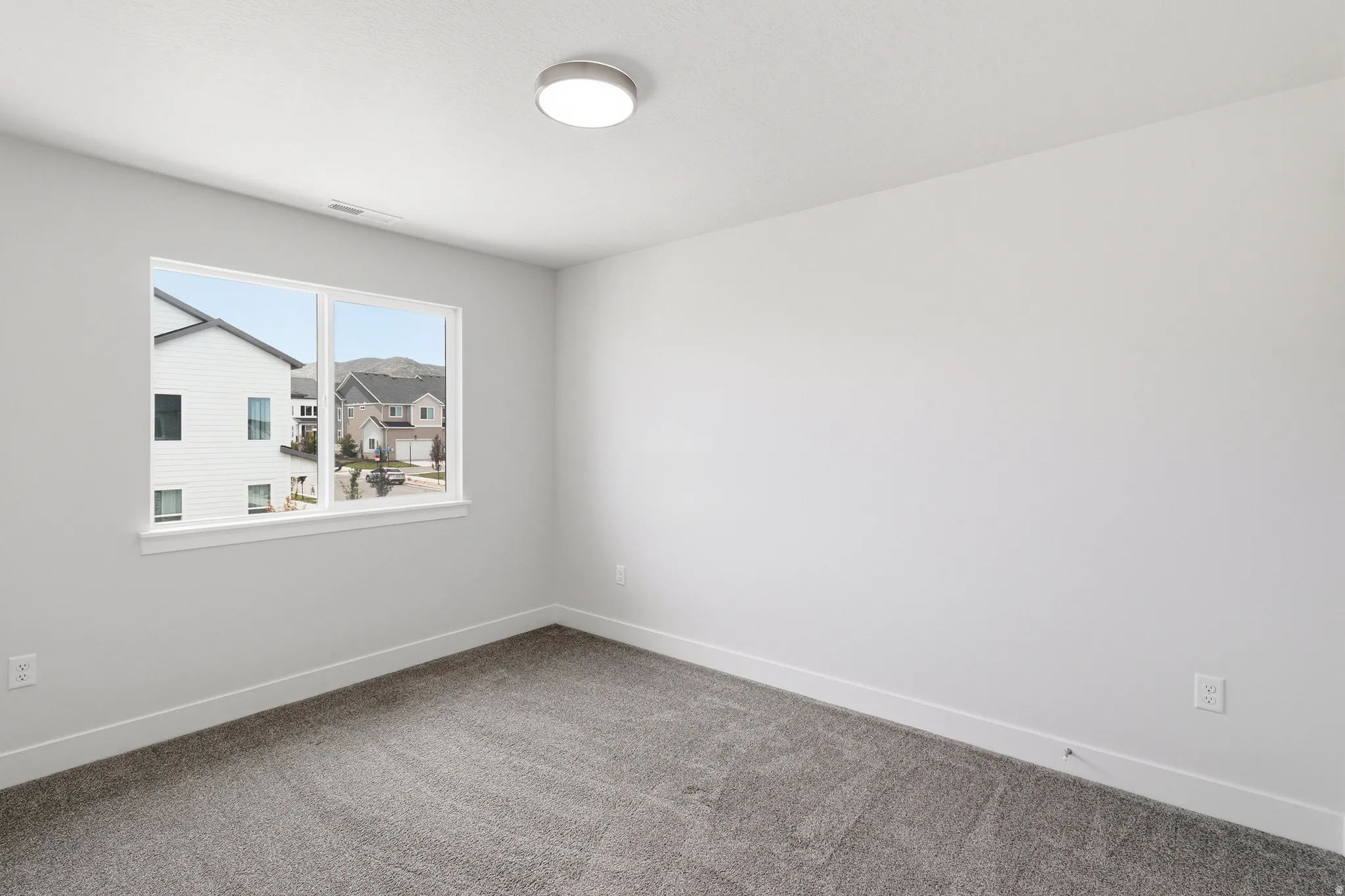 Bright interior space featuring a window with white trim, gray plush carpeting, white walls, and a contemporary ceiling light fixture