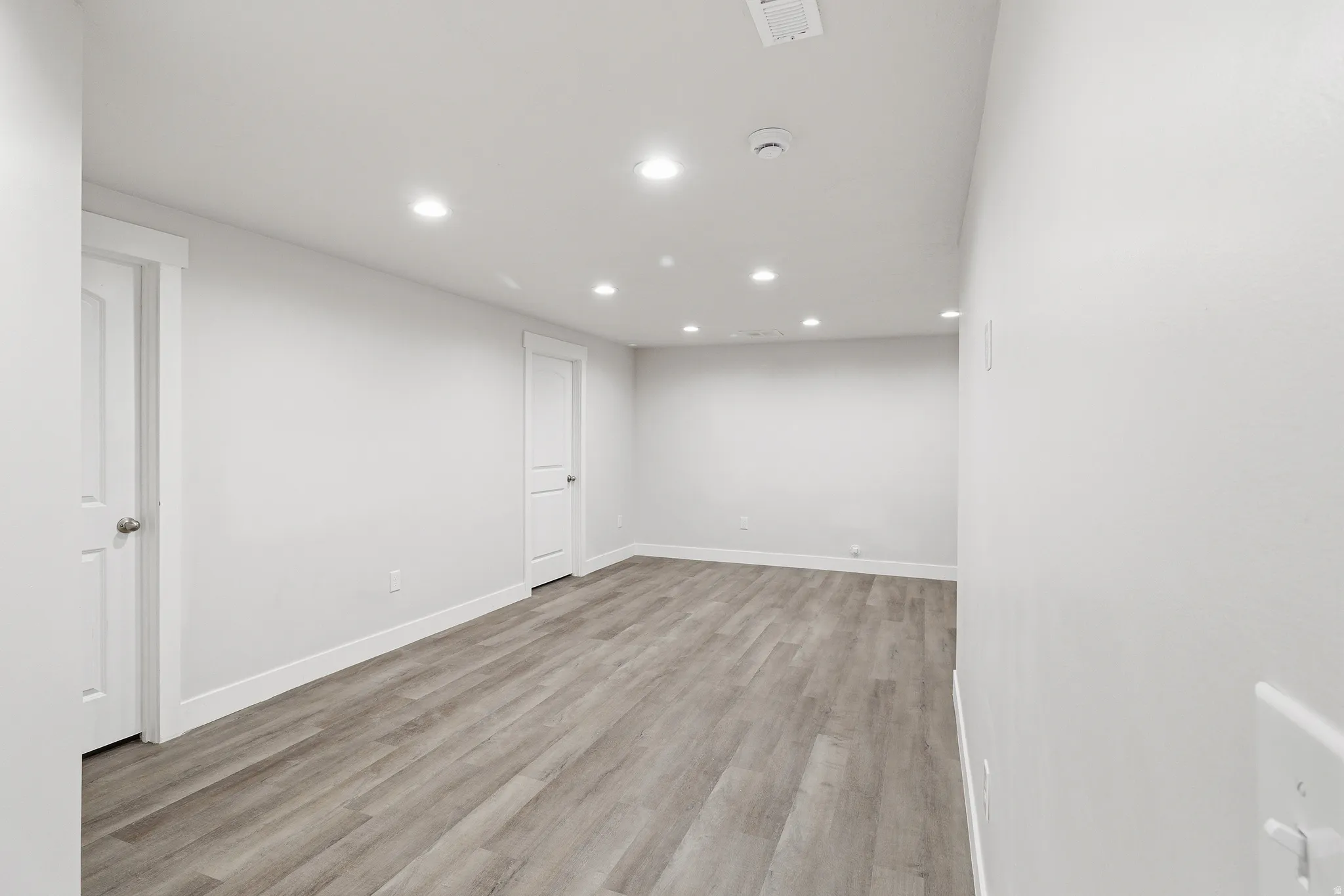 Spacious room featuring light wood-finish flooring, recessed lighting, and white walls