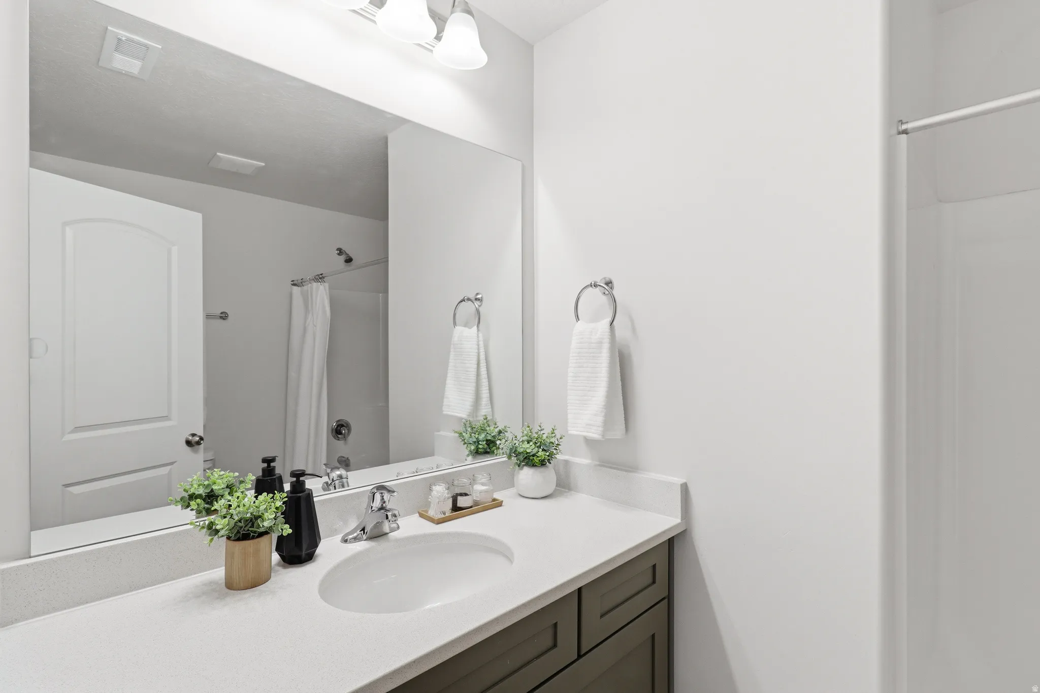 Bathroom vanity with a white countertop and integrated sink, chrome faucet, wood-finish cabinetry, and a large wall-mounted mirror