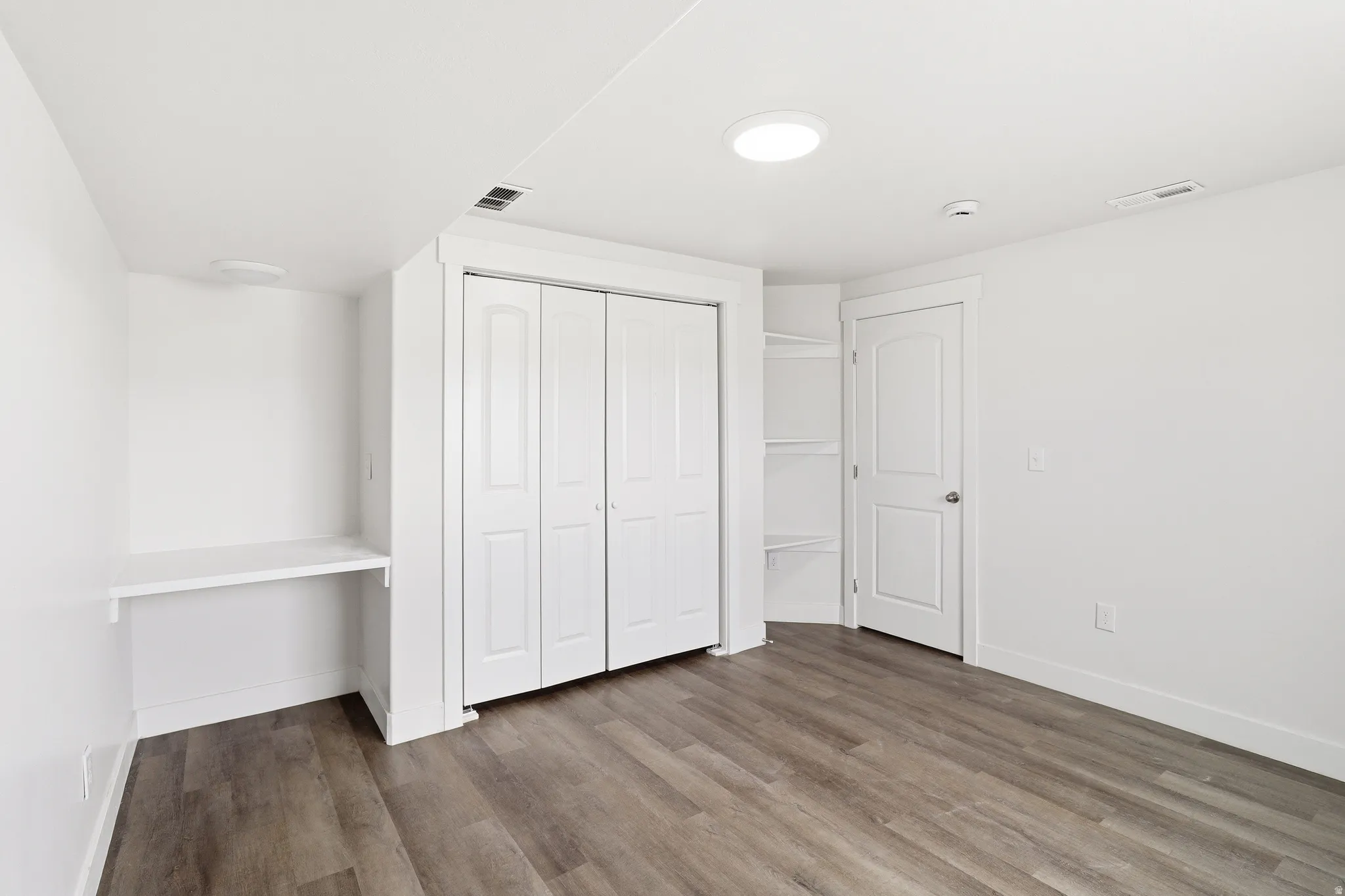 Spacious room featuring wood-finish flooring, a built-in desk, and a bi-fold closet