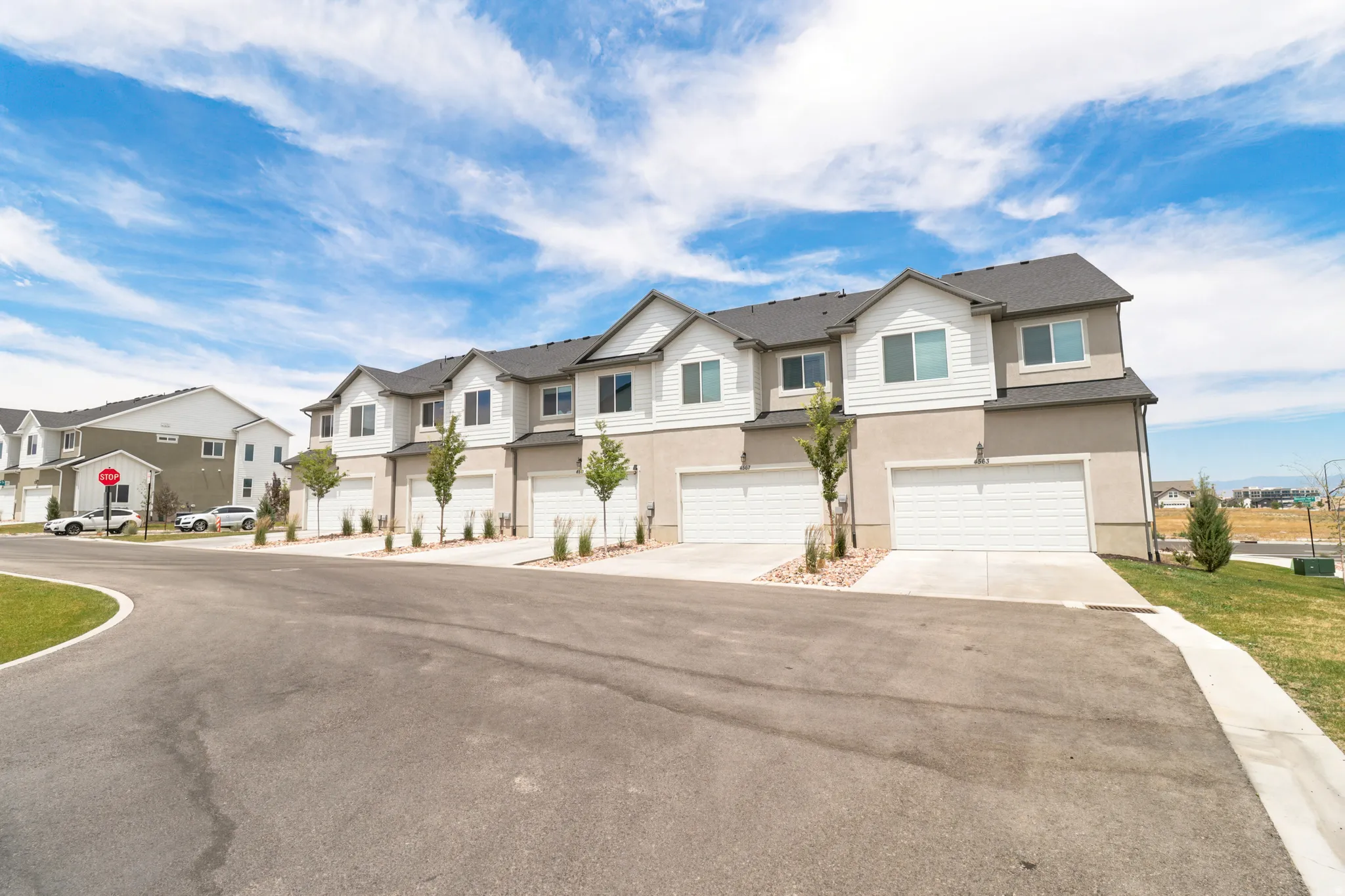 Contemporary townhome exterior featuring a two-tone facade, attached garages with white doors, and a paved driveway