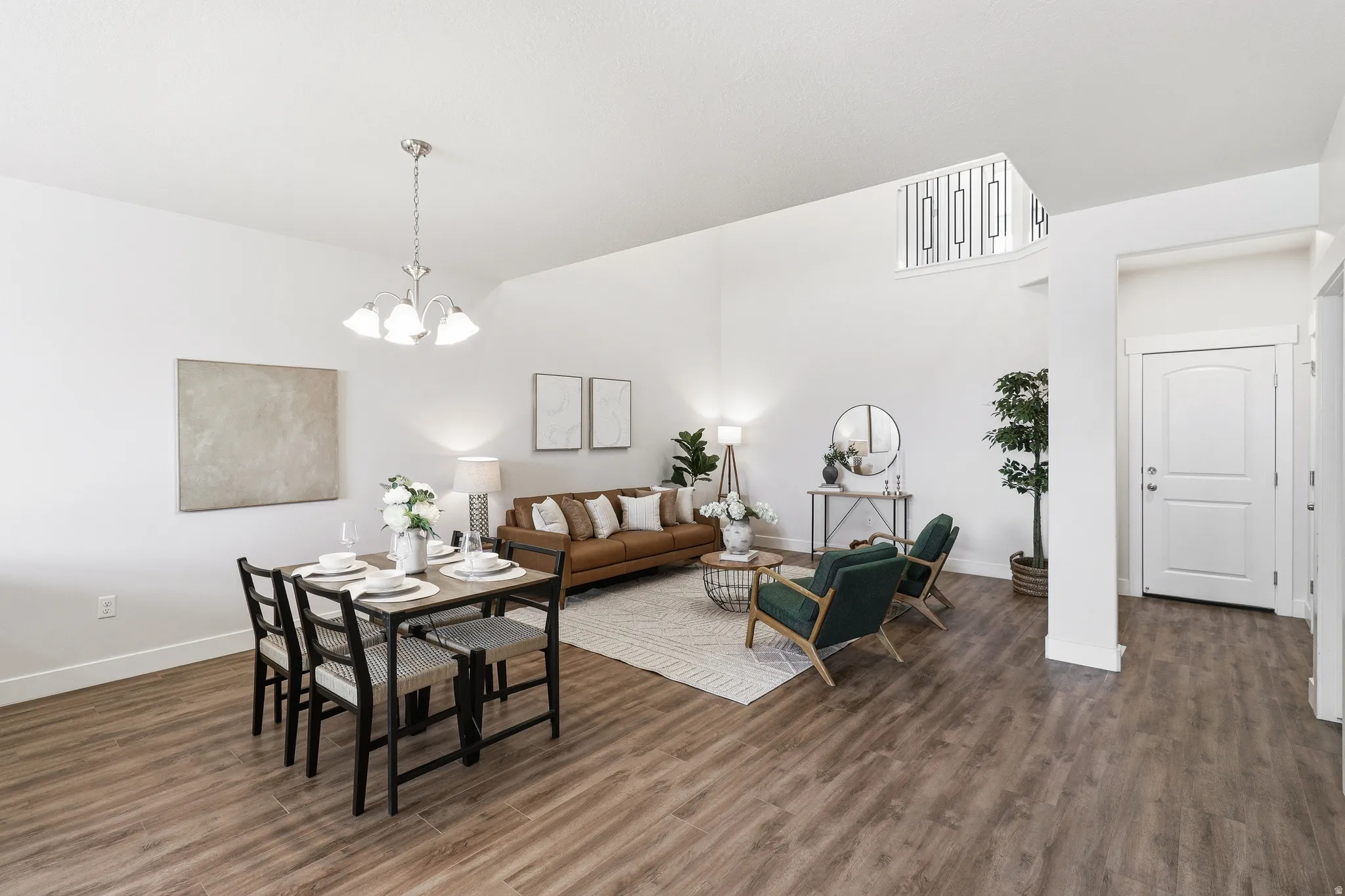 Open-concept living area featuring wood-finish flooring, high ceilings, a dining area with pendant lighting, and a partial view of an upper-level railing