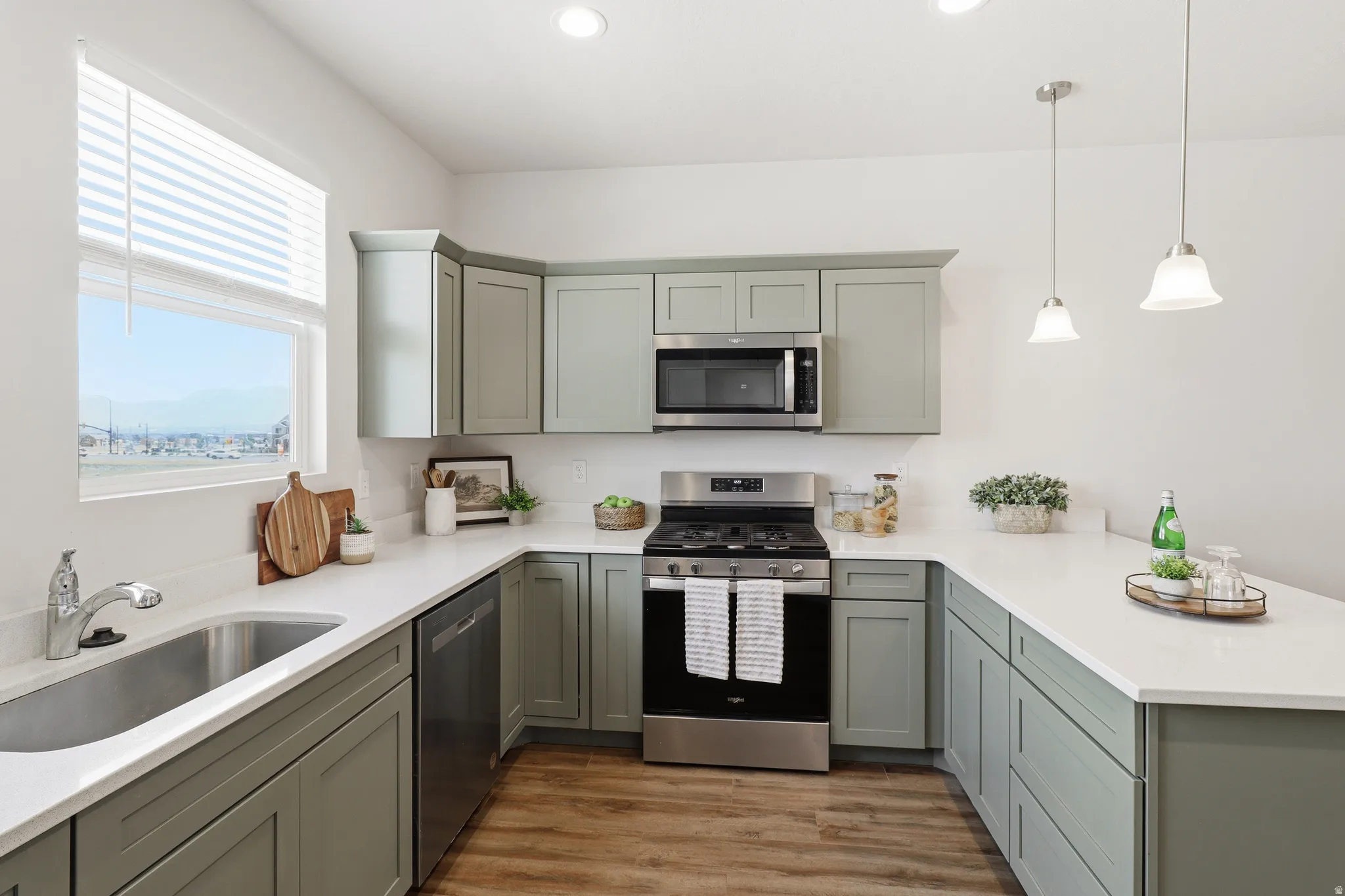 Kitchen featuring U-shaped cabinetry with a light green finish, stainless steel appliances, a stainless steel sink with a single-handle faucet, white countertops, and wood-finish flooring
