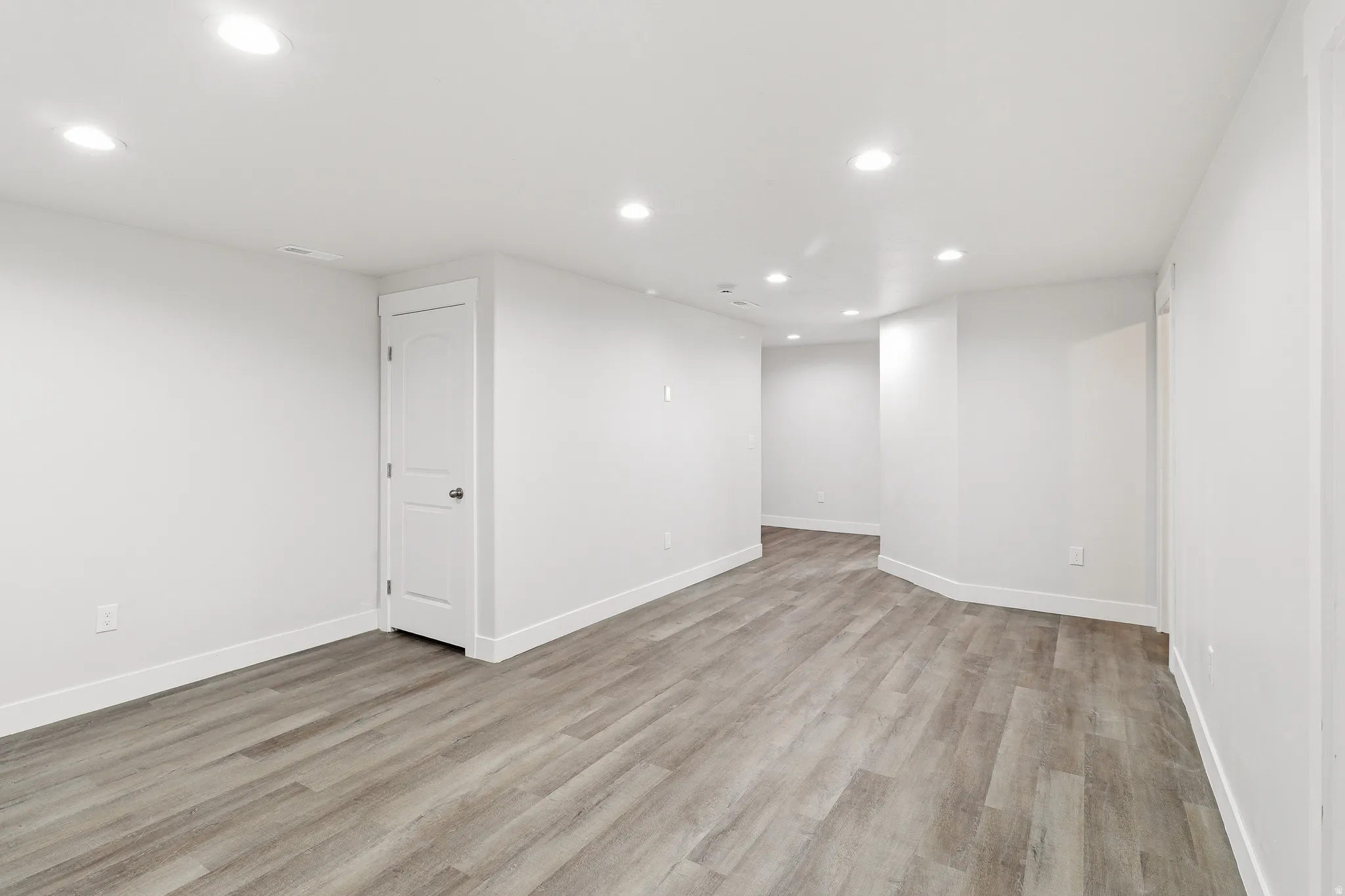 Spacious room featuring wood-finish flooring, white baseboards, recessed lighting, and crisp white walls