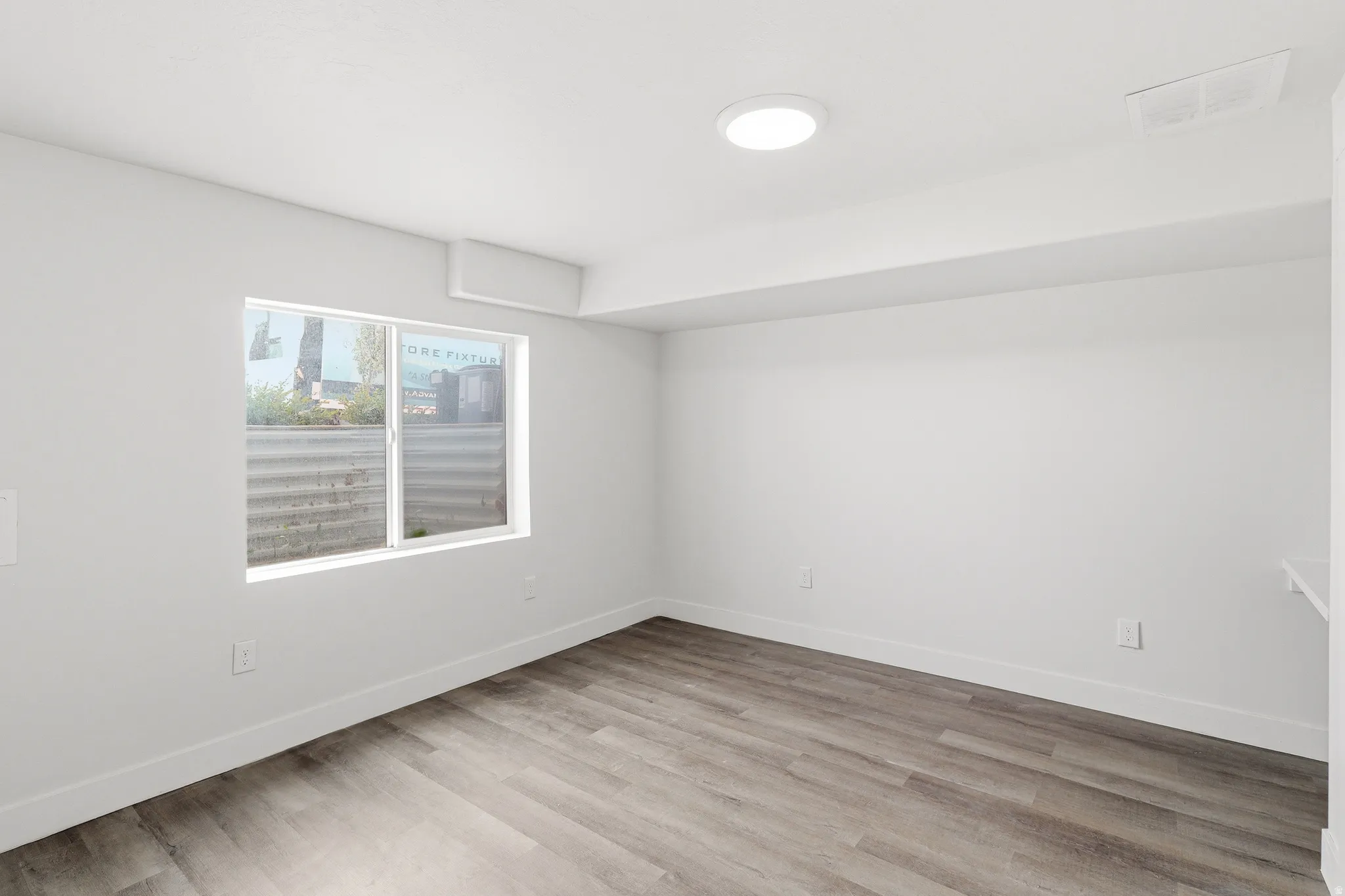 Spacious room featuring wood-finish flooring, white walls, and a recessed ceiling light