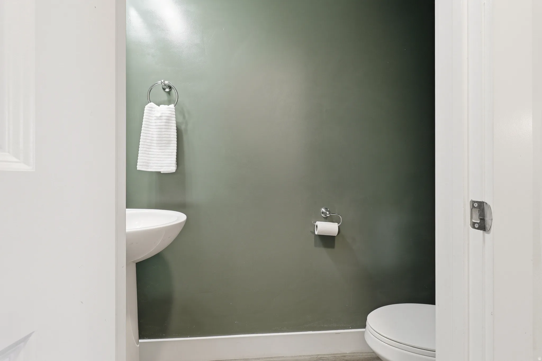 Compact powder room featuring a white pedestal sink, a toilet, a chrome towel ring, and a chrome toilet paper holder
