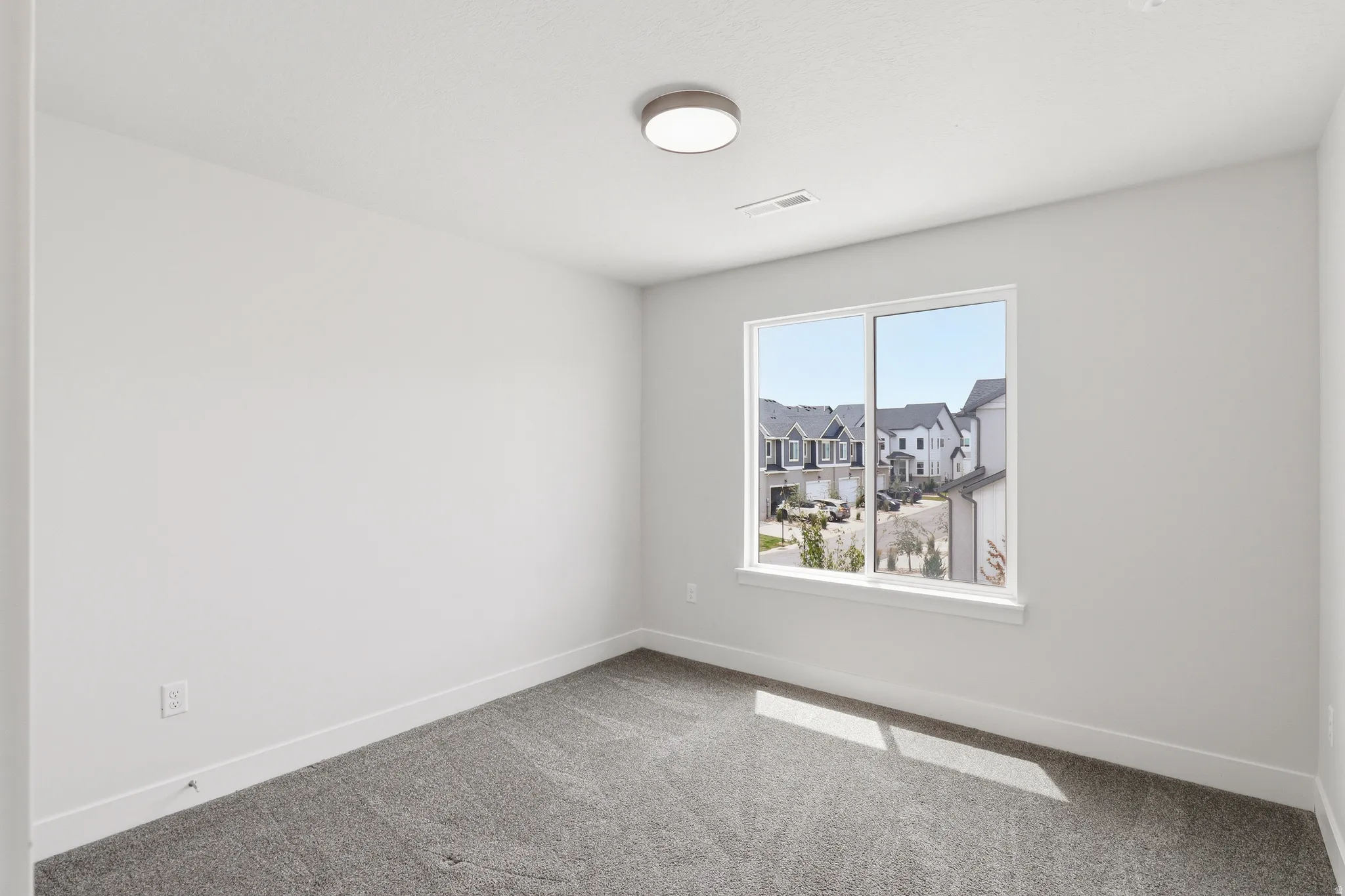 Bright room featuring a large window, soft gray carpeting, white walls, and a modern ceiling light fixture