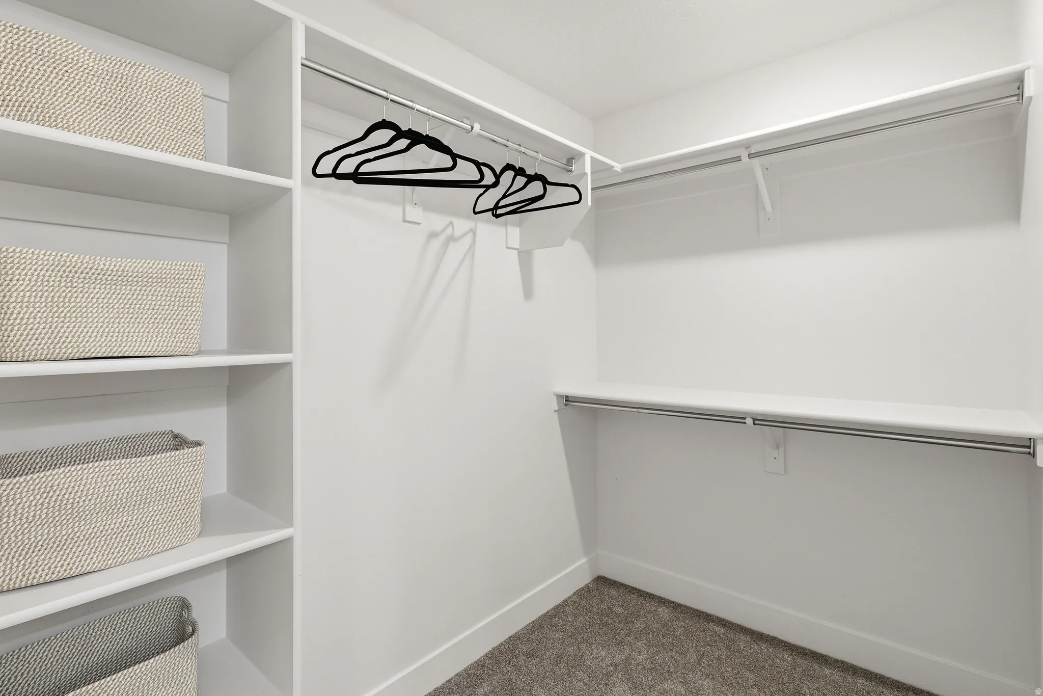 Walk-in closet featuring built-in shelving, white walls, white baseboards, wall-mounted hanging rods, and grey carpet flooring