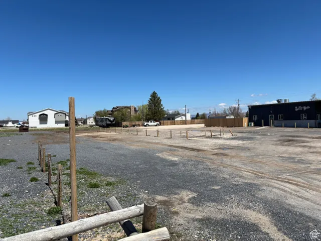 Expansive gravel lot featuring a partial split rail fence, clear boundaries, and existing perimeter structures