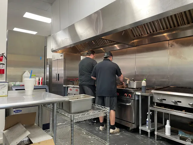 Commercial kitchen featuring stainless steel appliances, large ventilation hood, and extensive counter space