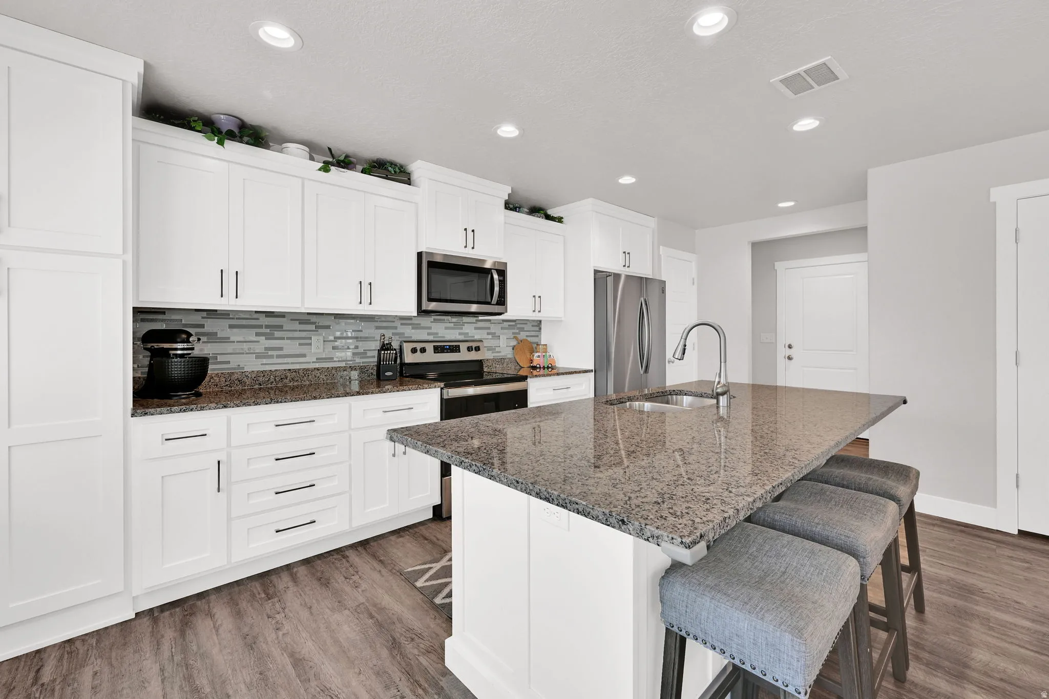 Modern kitchen featuring white shaker cabinetry, granite countertops, stainless steel appliances, a tile backsplash, and LVP flooring
