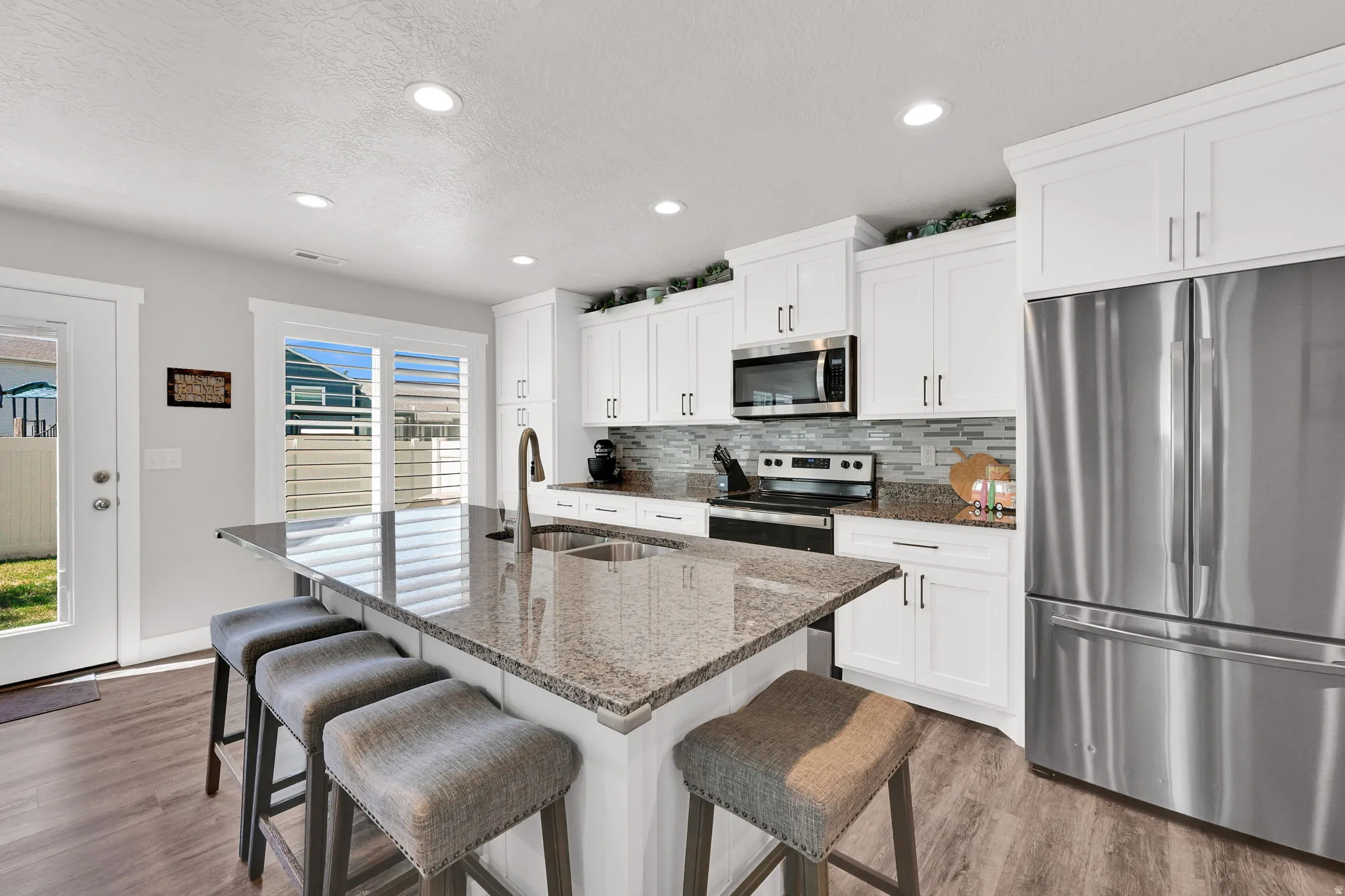 Modern kitchen featuring white shaker cabinetry, granite countertops, stainless steel appliances, a tile backsplash, and LVP flooring