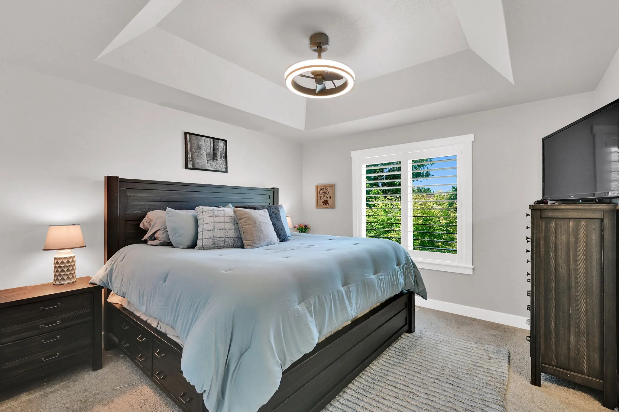 Primary Bedroom- featuring primary en suite, walk in closet, window with plantation shutters, ceiling fan with integrated lighting, carpet and light-toned wall paint
