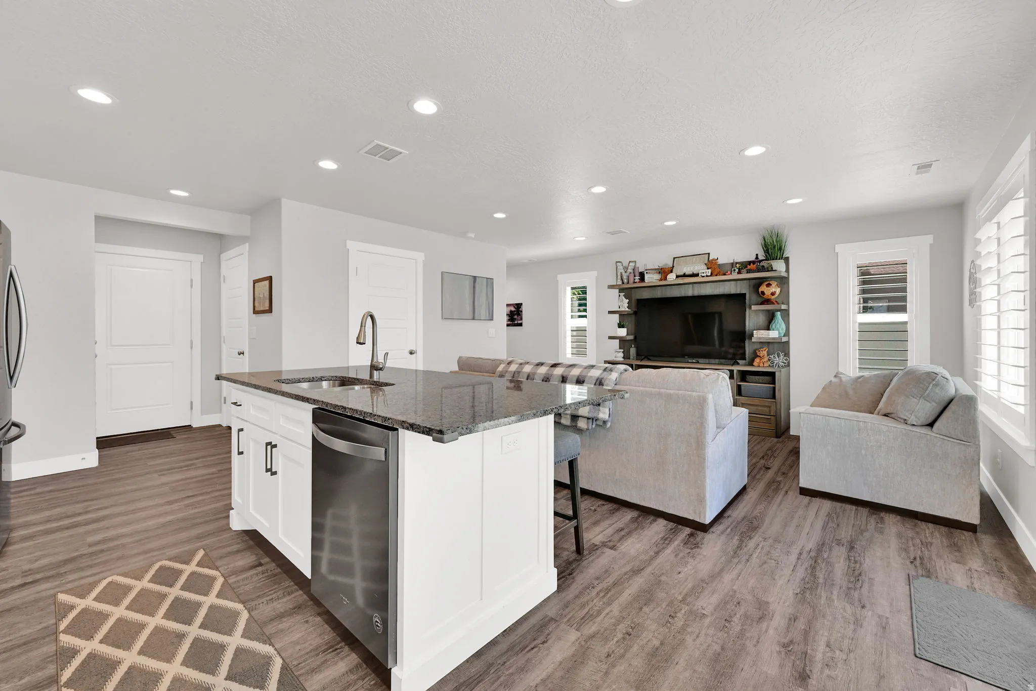 Open-concept living space/kitchen  featuring LVP flooring, recessed lighting, and white plantation shutters