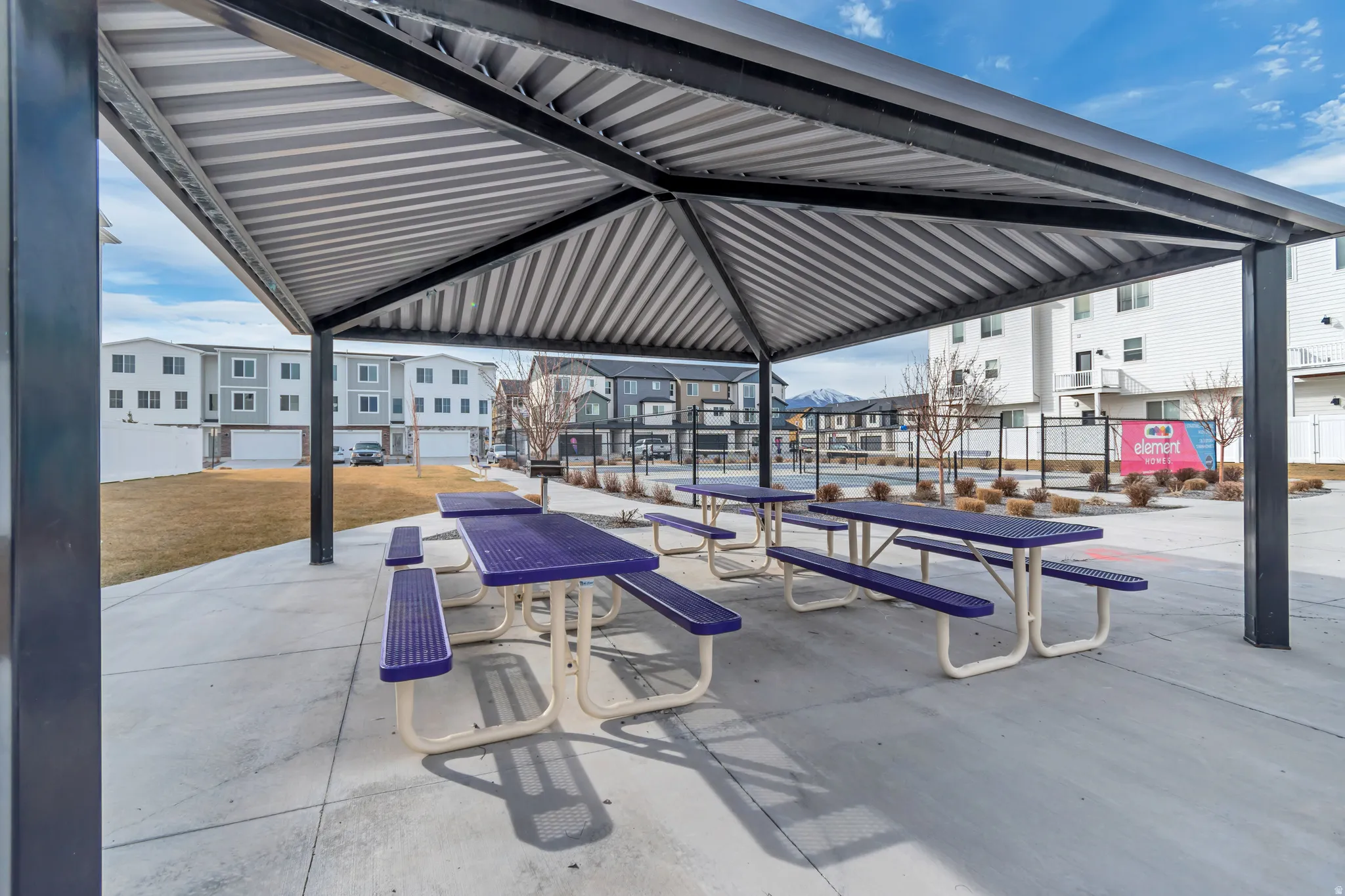 Covered outdoor patio area featuring multiple picnic tables with purple seating