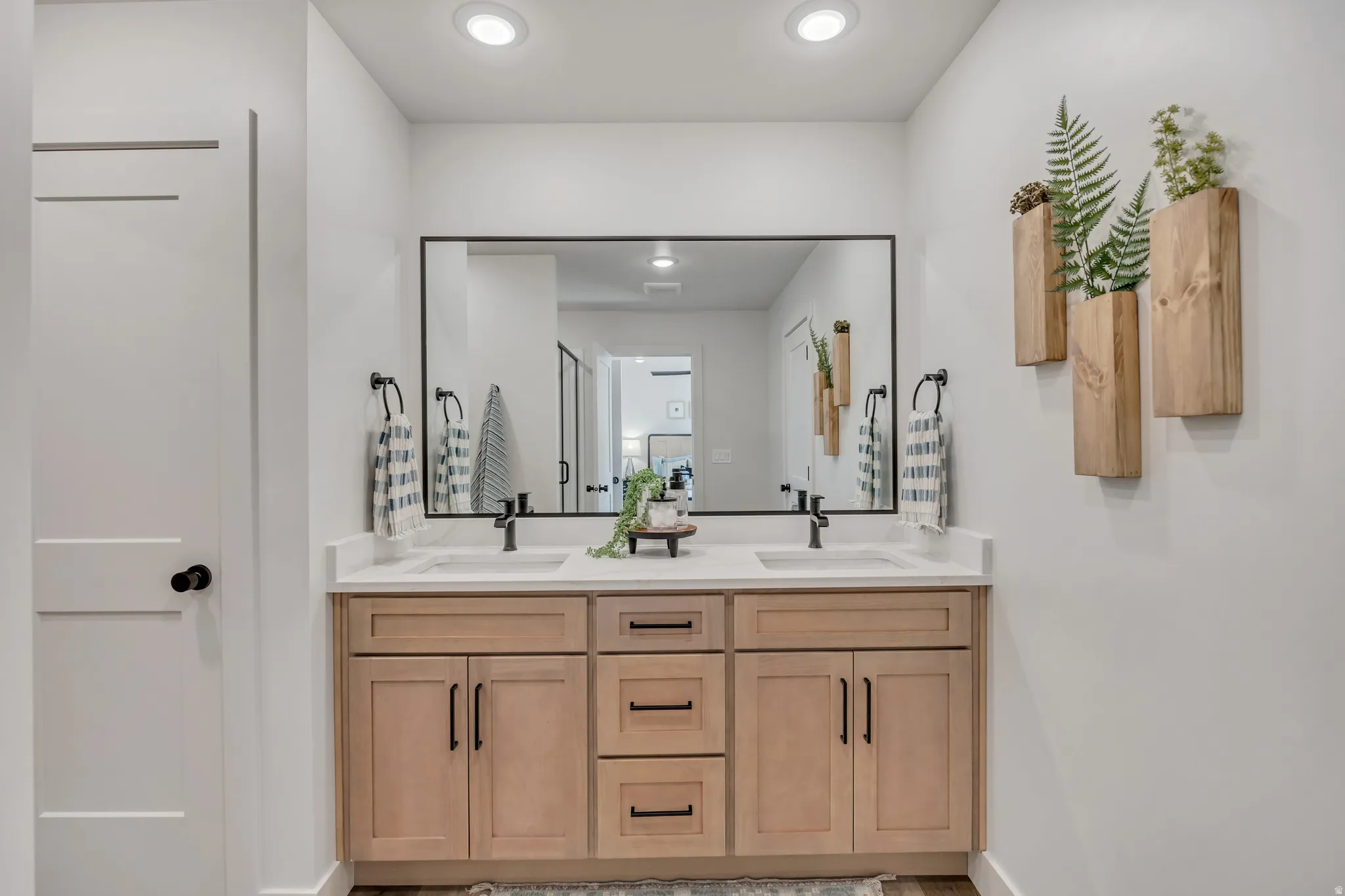 Dual vanity with light wood-finish cabinetry, black hardware, and an expansive framed mirror