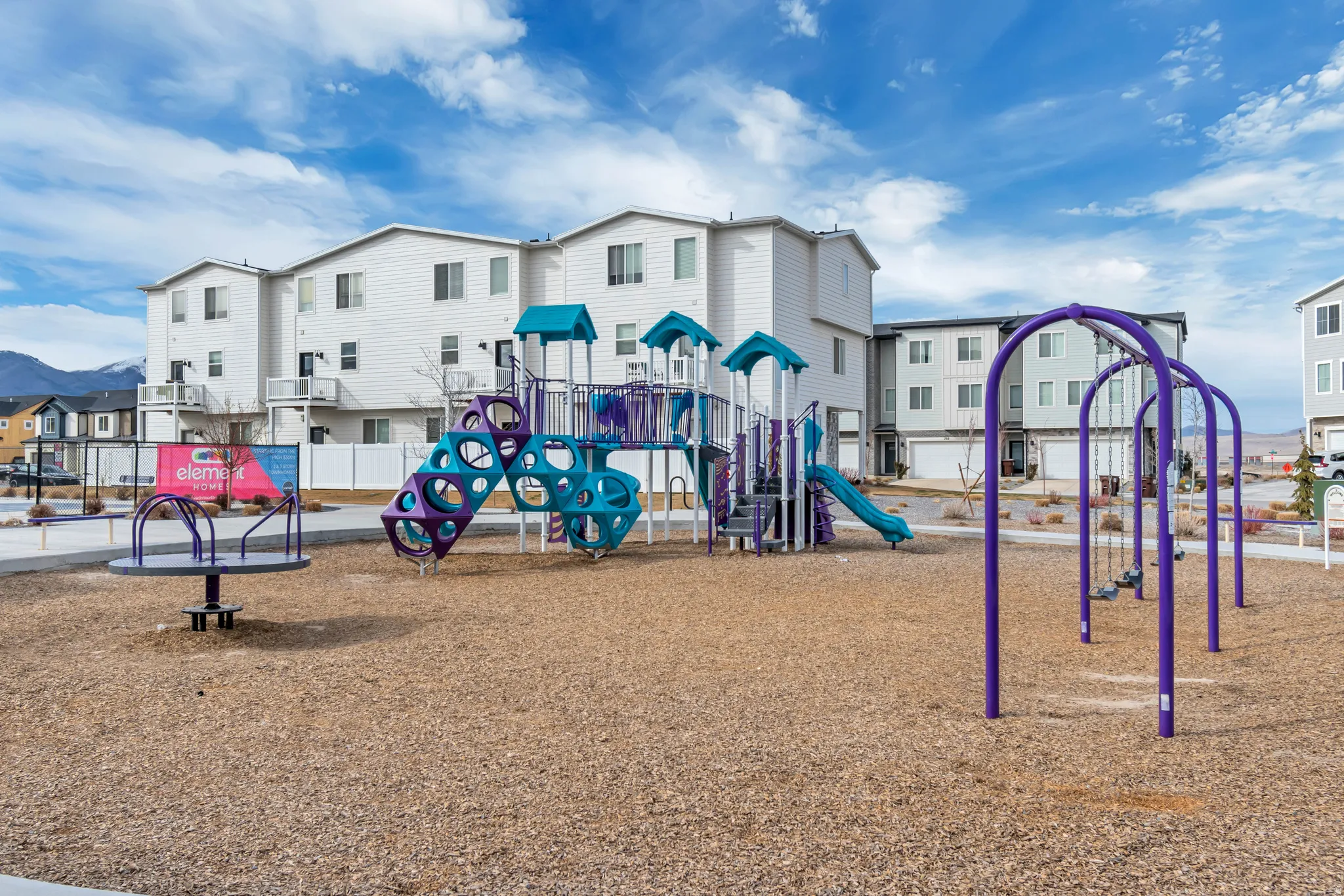 Community playground featuring a multi-level play structure, swings, and a merry-go-round