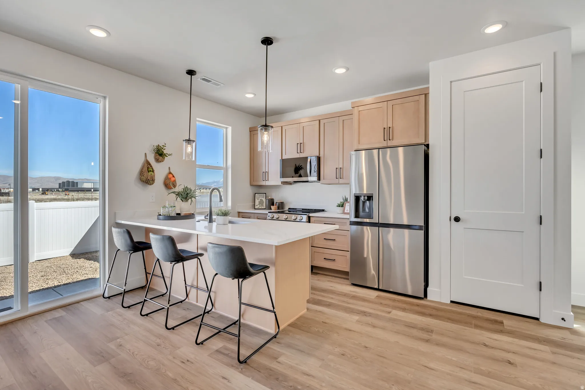 Modern kitchen featuring a central island with countertop seating, light wood-finish cabinetry, stainless steel appliances, and wood-finish flooring