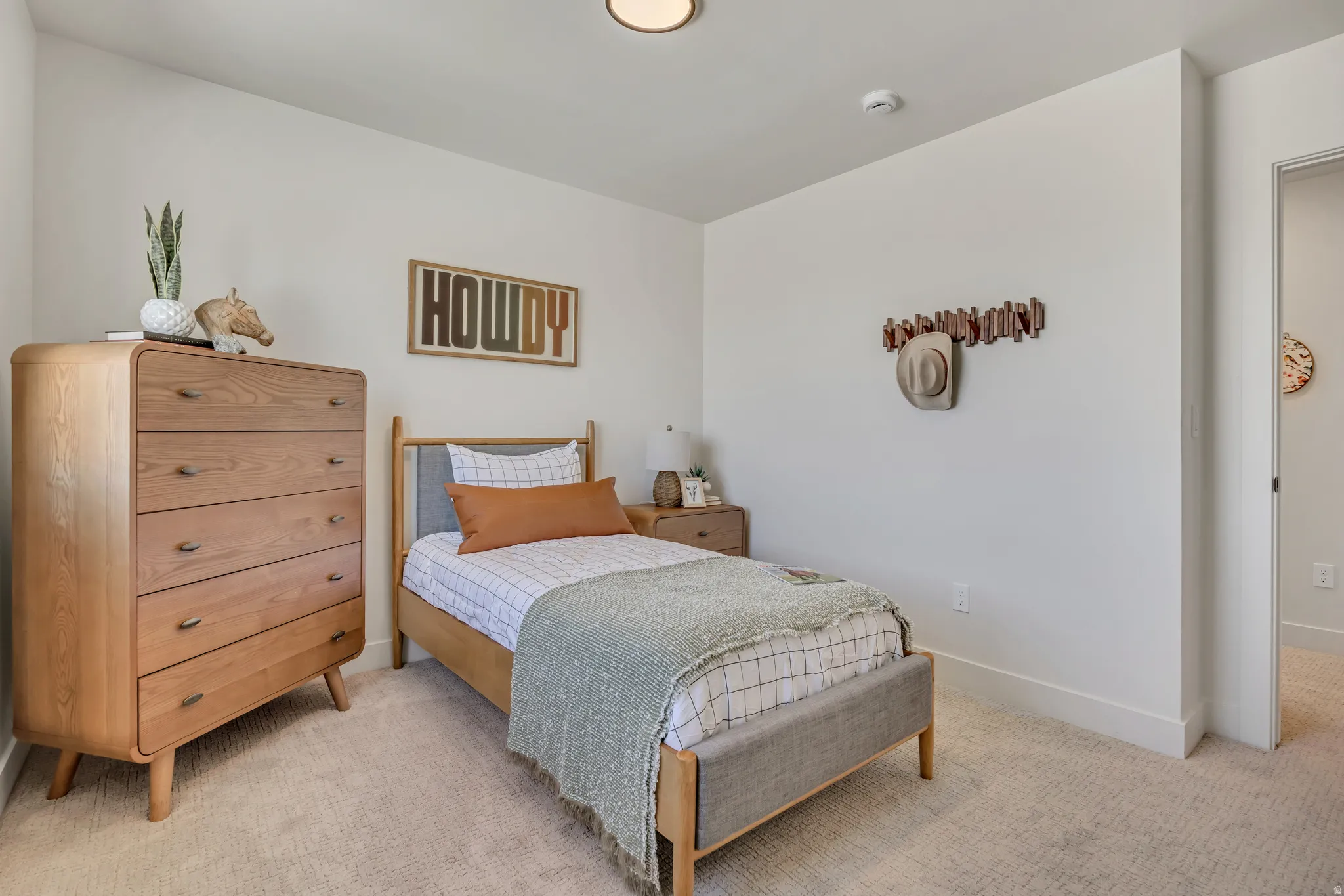 Neutral wall finishes and light-toned carpeting complement the natural wood-frame bed with an upholstered headboard