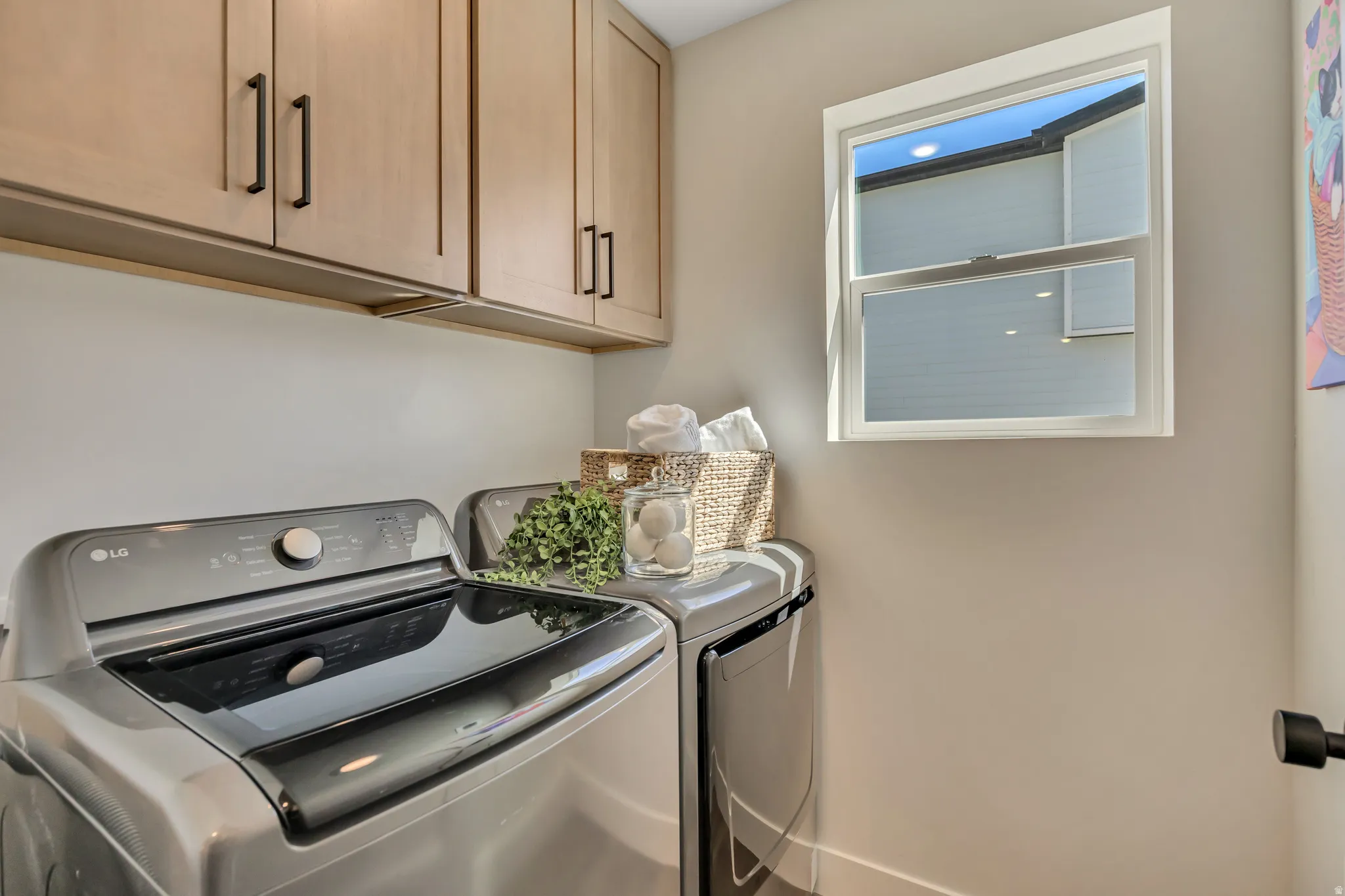 Laundry area featuring light wood-finish cabinetry with matte black hardware, a single-hung window, and neutral wall paint
