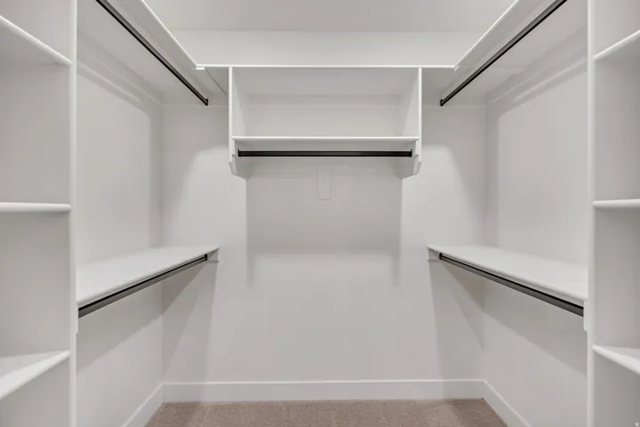 Walk-in closet featuring built-in shelving, multiple hanging rods, and neutral-toned carpeting