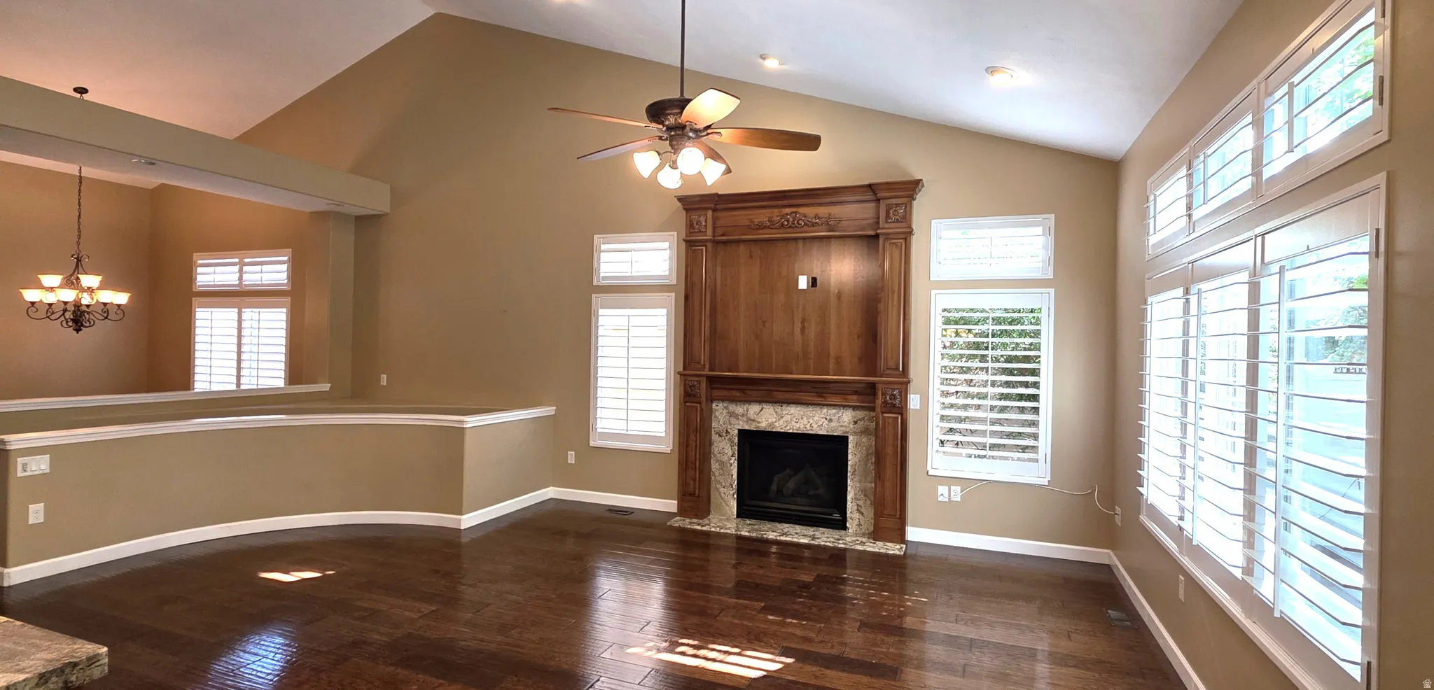 Vaulted ceilings, wood-finish flooring, a fireplace with a stone surround, an integrated wood-finish media cabinet, and plantation shutters