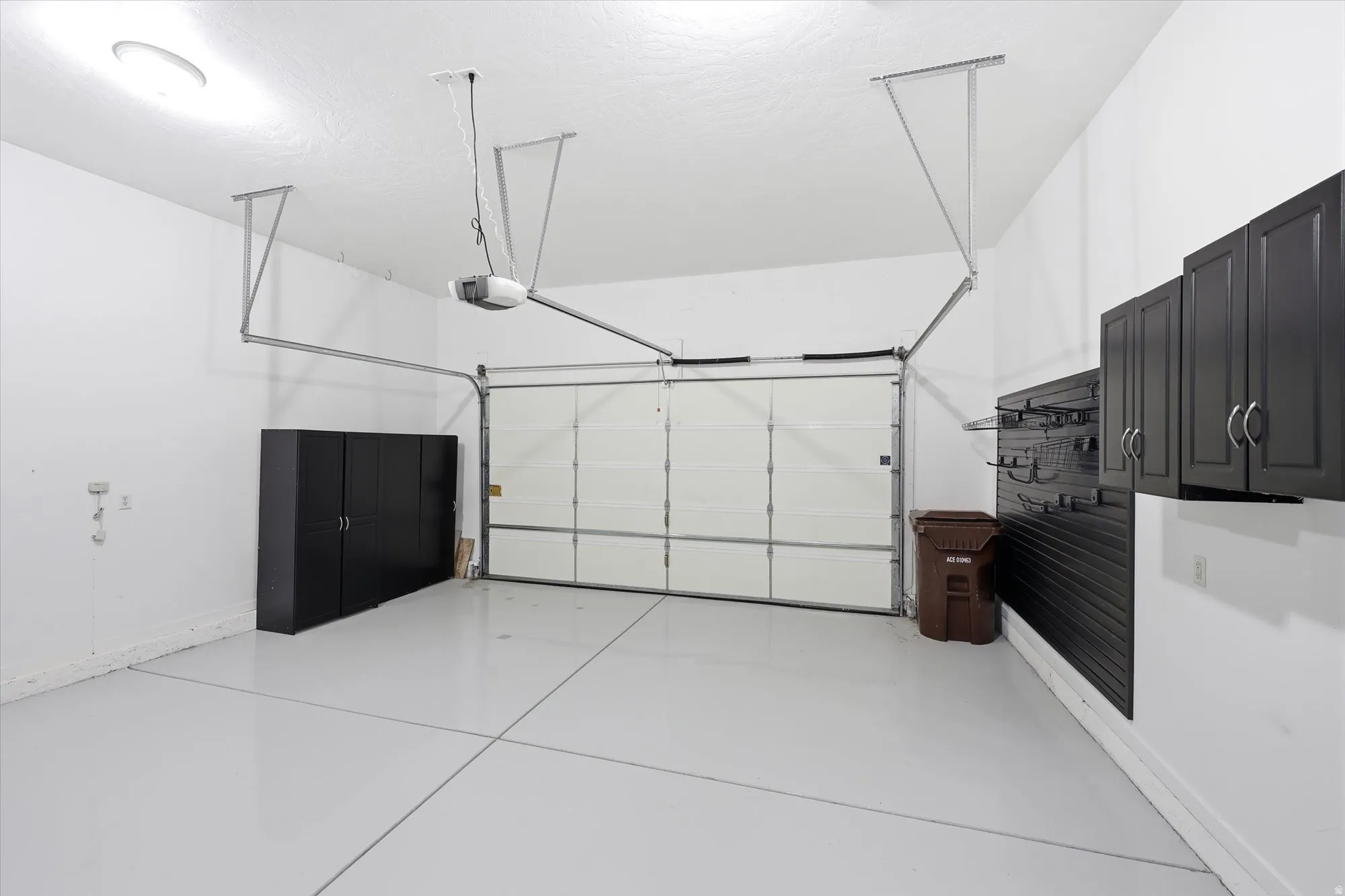 Spacious garage featuring a white overhead door, epoxy floor, built-in storage cabinets, and wall-mounted shelving system