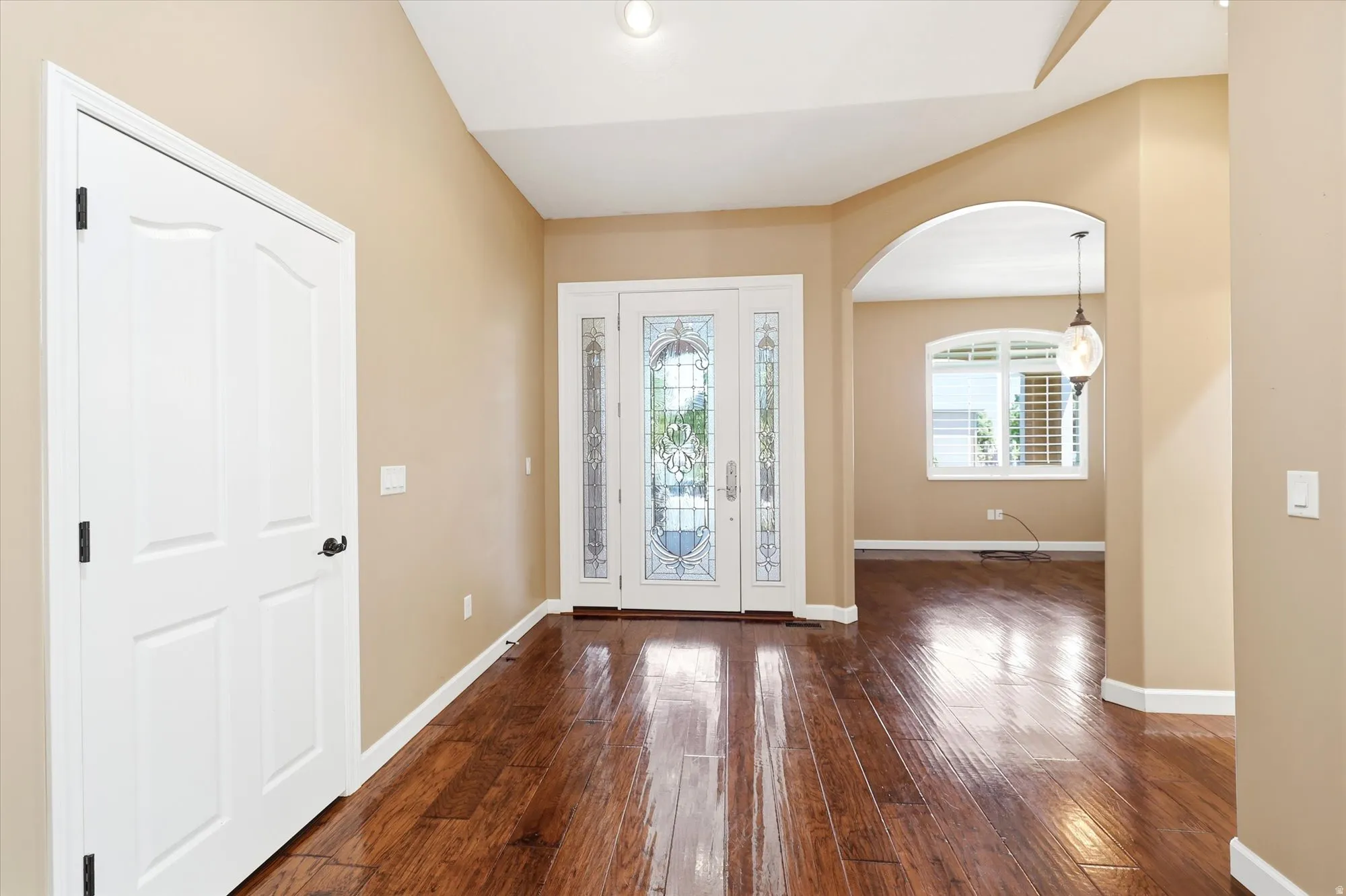 Entryway featuring wood-finish flooring, a decorative glass paneled double door, and an arched doorway leading to an office
