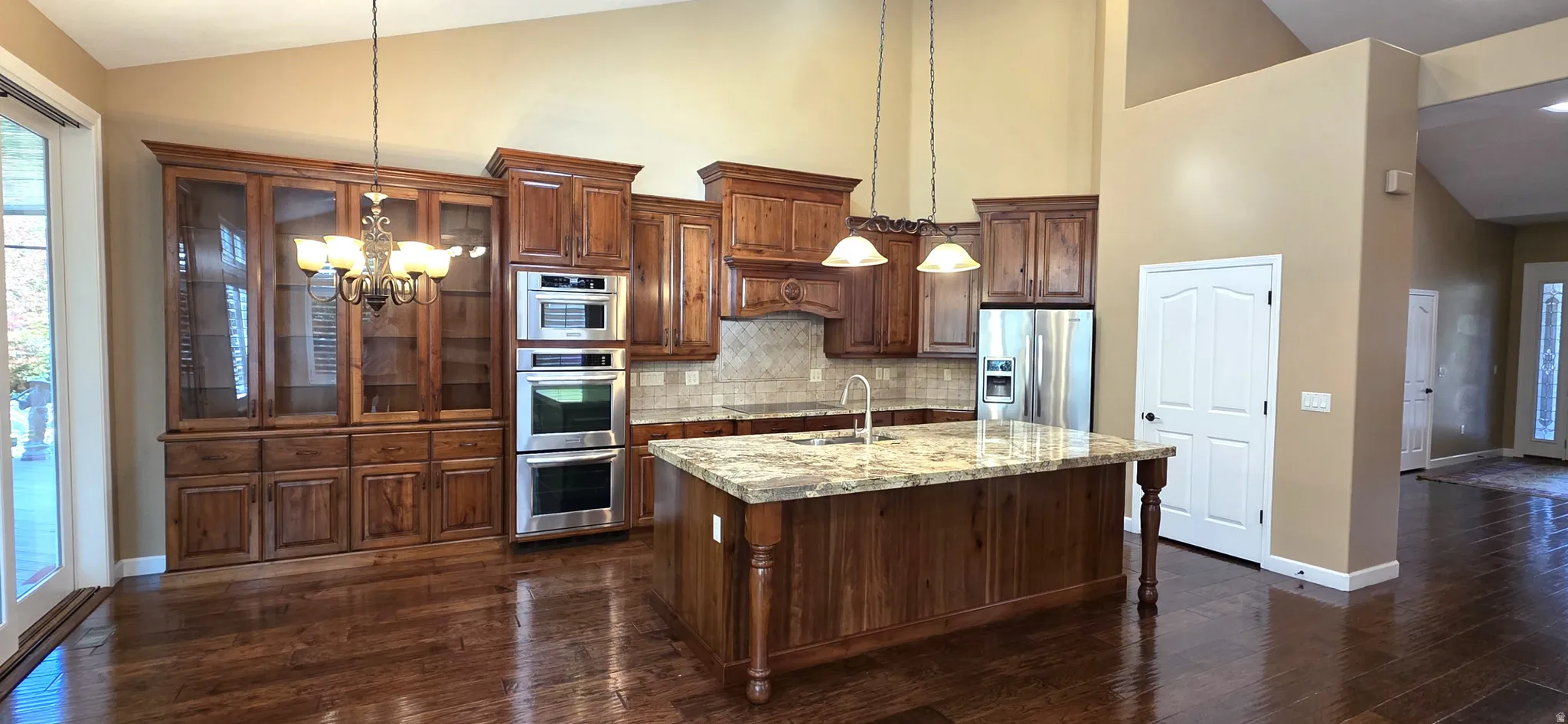 Kitchen featuring wood-finish cabinetry, a large center island with a stone countertop, stainless steel double ovens, and wood-finish flooring