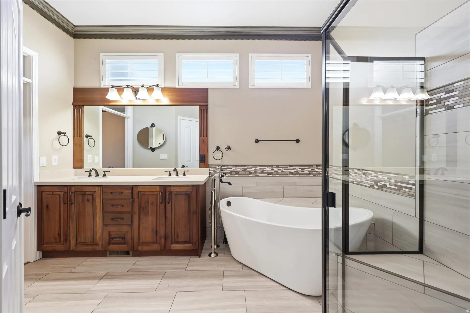 Spacious bathroom featuring a double vanity with wood cabinetry, a large frameless mirror, and a standalone soaking tub
