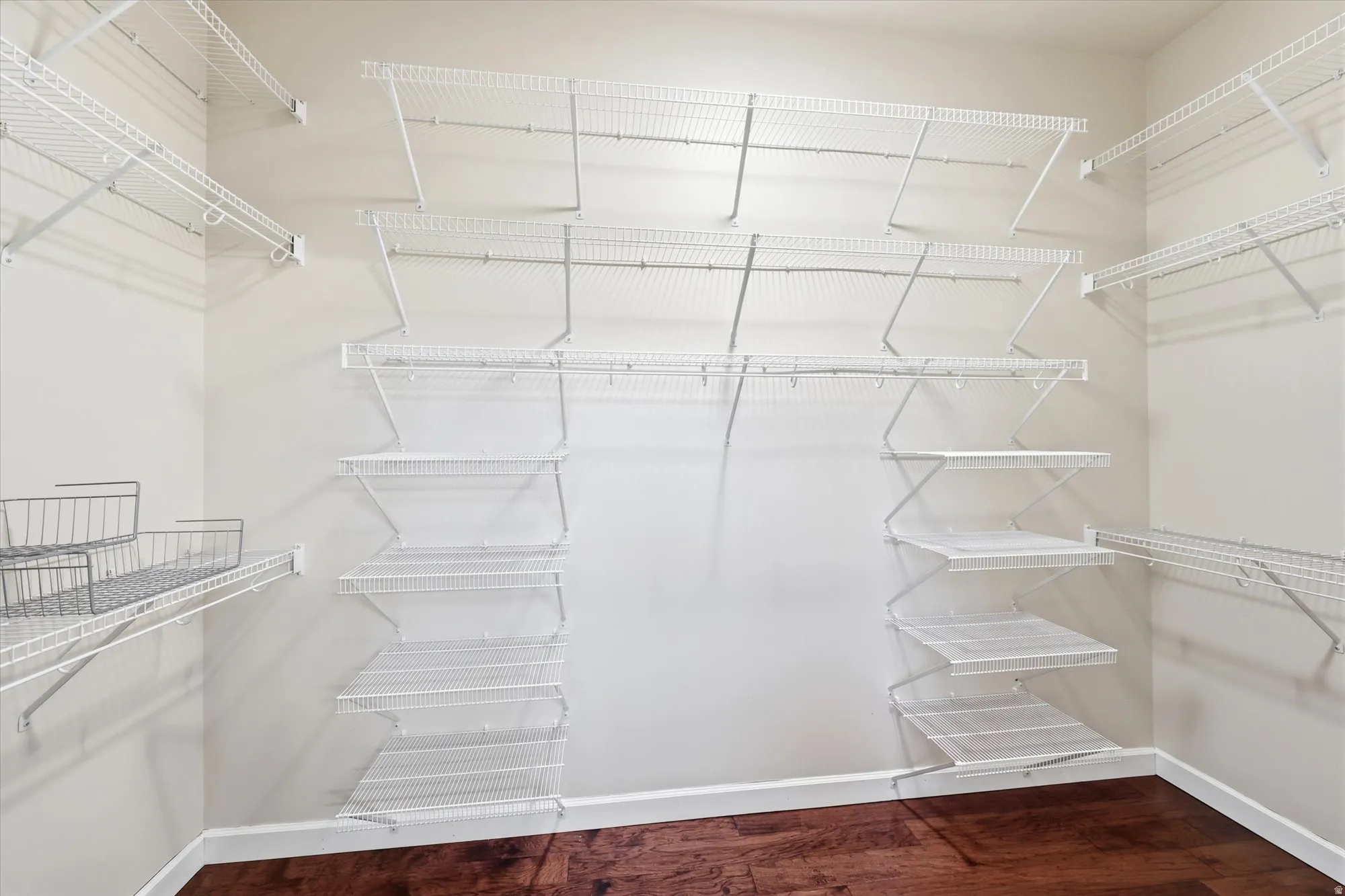 Walk-in closet featuring extensive wire shelving, multiple hanging rods, corner shelving units, wood-finish flooring, and white baseboards