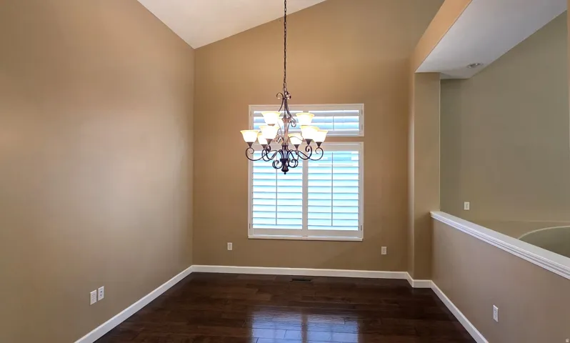 Vaulted ceiling, dark wood-finish flooring, plantation shutters, chandelier, and architectural half-wall
