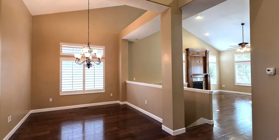 Vaulted ceilings, dark wood-finish flooring, plantation shutters, and an ornate chandelier