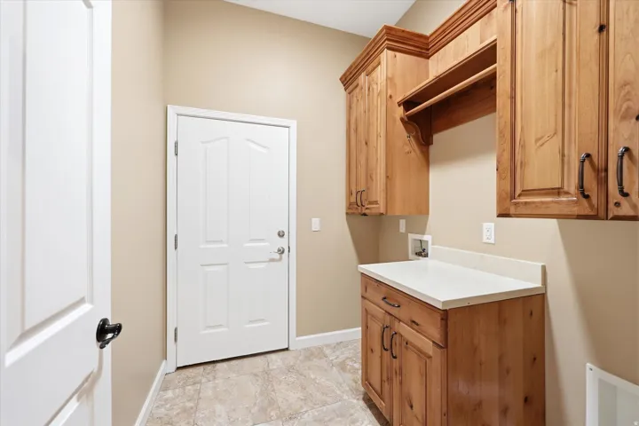 Utility room with tile flooring, natural wood cabinetry, a light-toned countertop, and a built-in drying rack