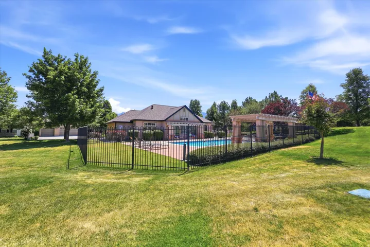 Expansive green lawn bordering a property with a swimming pool, pergola, and iron fencing