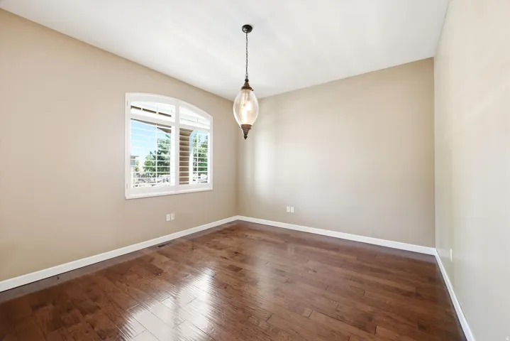 Office featuring wood-finish flooring, an arched window with louvered shutters, a ceiling-mounted light fixture, and neutral wall tones
