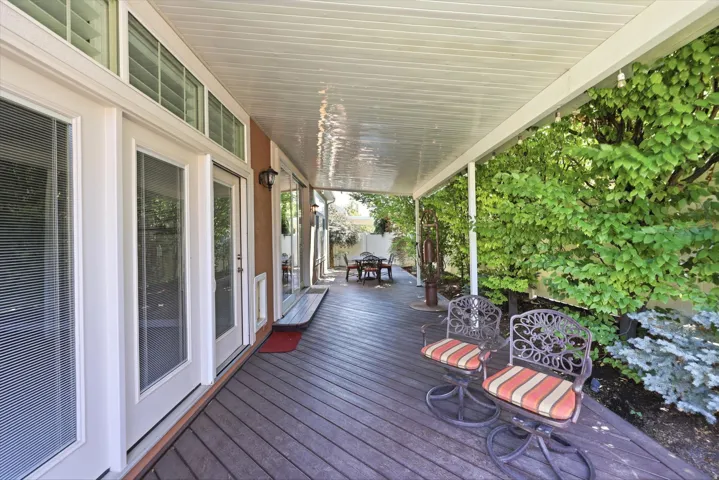 Covered patio featuring multiple French doors with transom windows, a stucco exterior, and surrounding mature trees