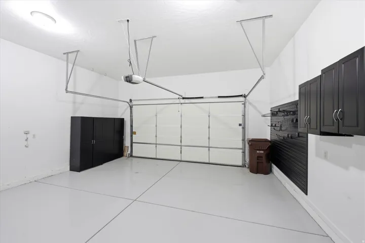 Spacious garage featuring a white overhead door, epoxy floor, built-in storage cabinets, and wall-mounted shelving system