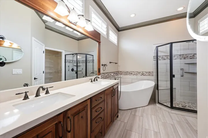 Main Bathroom featuring a dual vanity with a light-colored countertop and wood-finish cabinetry, a freestanding soaking tub, and a glass-enclosed shower with a mosaic tile accent and pebble flooring