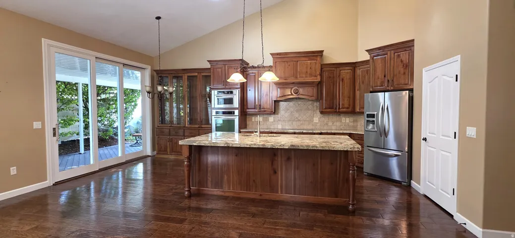Vaulted ceilings, wood-finish flooring, custom wood cabinetry, a center island with a stone countertop, and stainless steel appliances